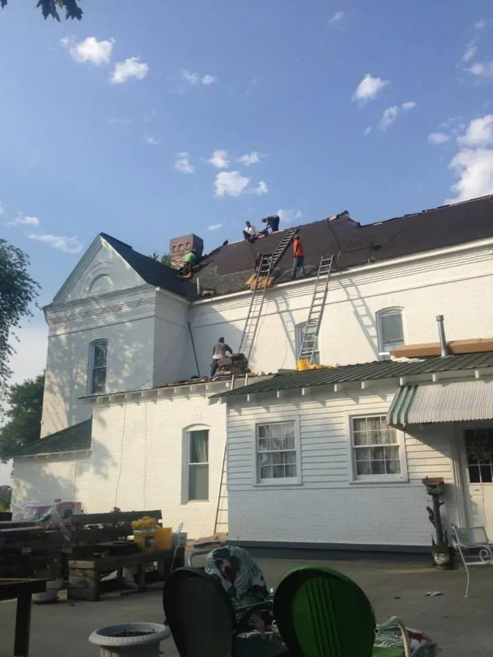 A group of people are working on the roof of a white house.