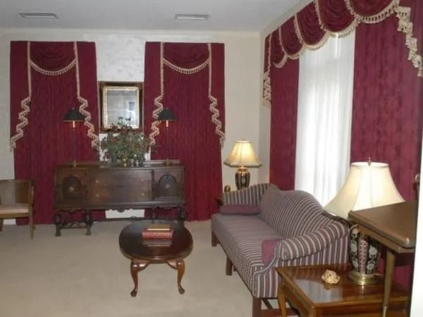 Living room with maroon curtains, antique furniture, and lamps.