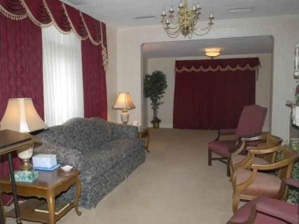 Living room with burgundy curtains, sofa, lamps, and chairs; open doorway to another room.