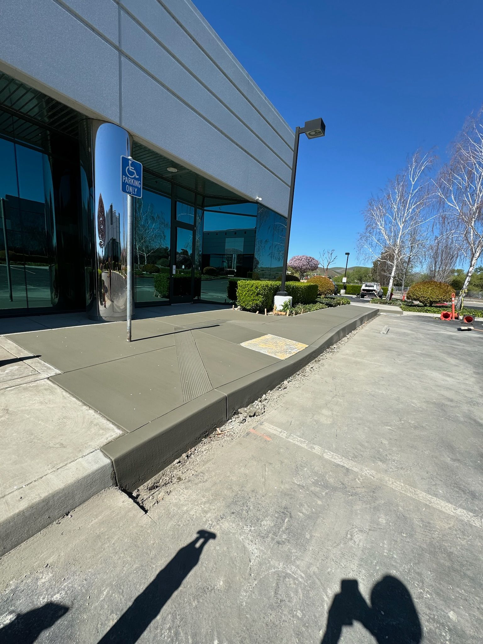 A shadow of a person is cast on the sidewalk in front of a building.