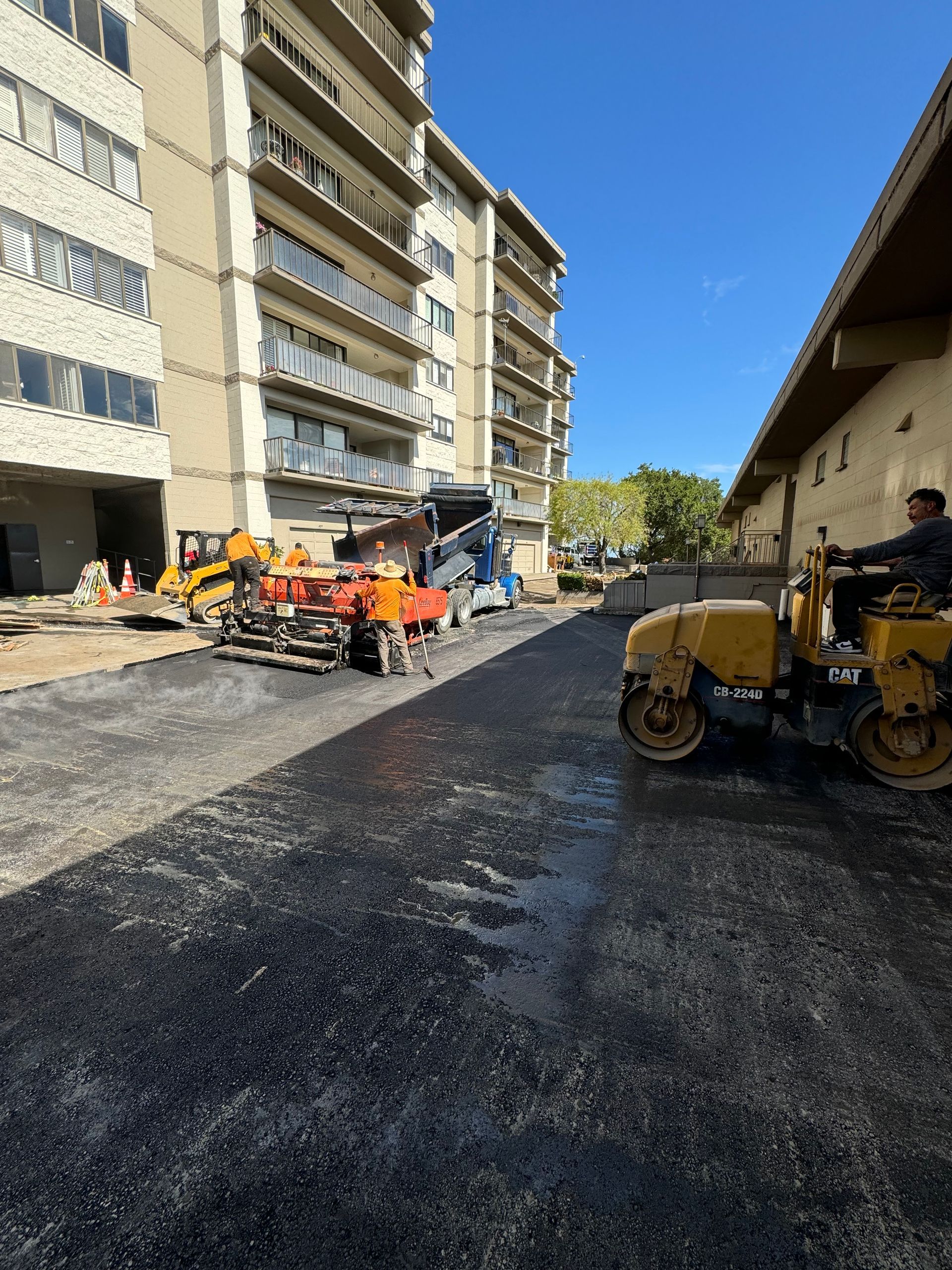 A man is driving a yellow roller on a road in front of a building.