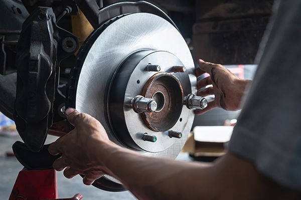 Hands working on a car brake rotor and caliper in a garage