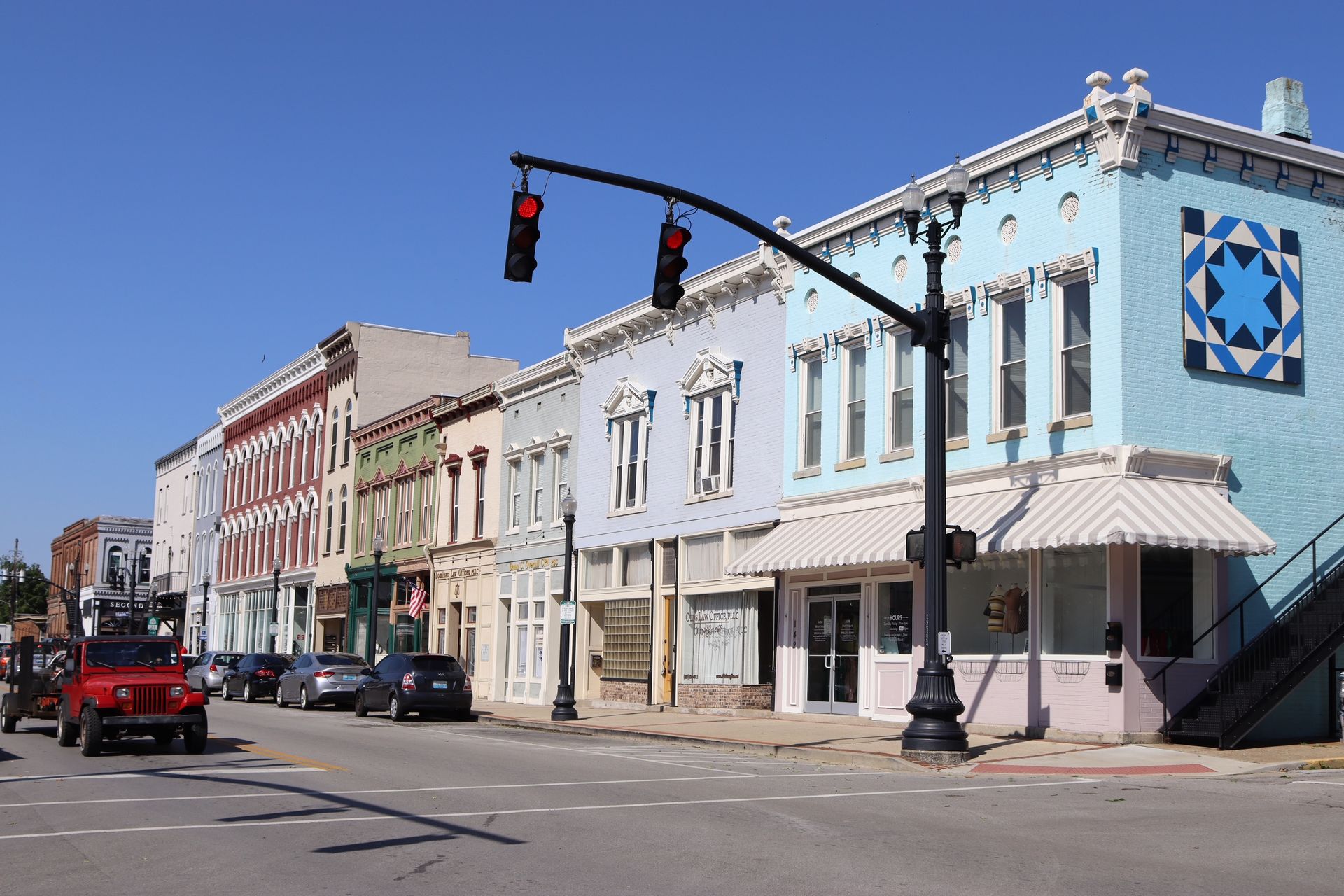 A red jeep is driving down a street in front of a row of buildings