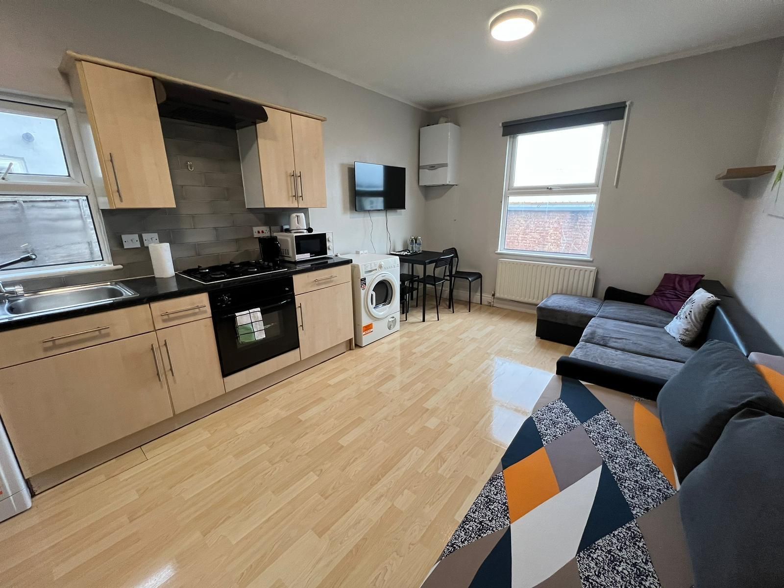 A living room with a couch and a kitchen with a washing machine.