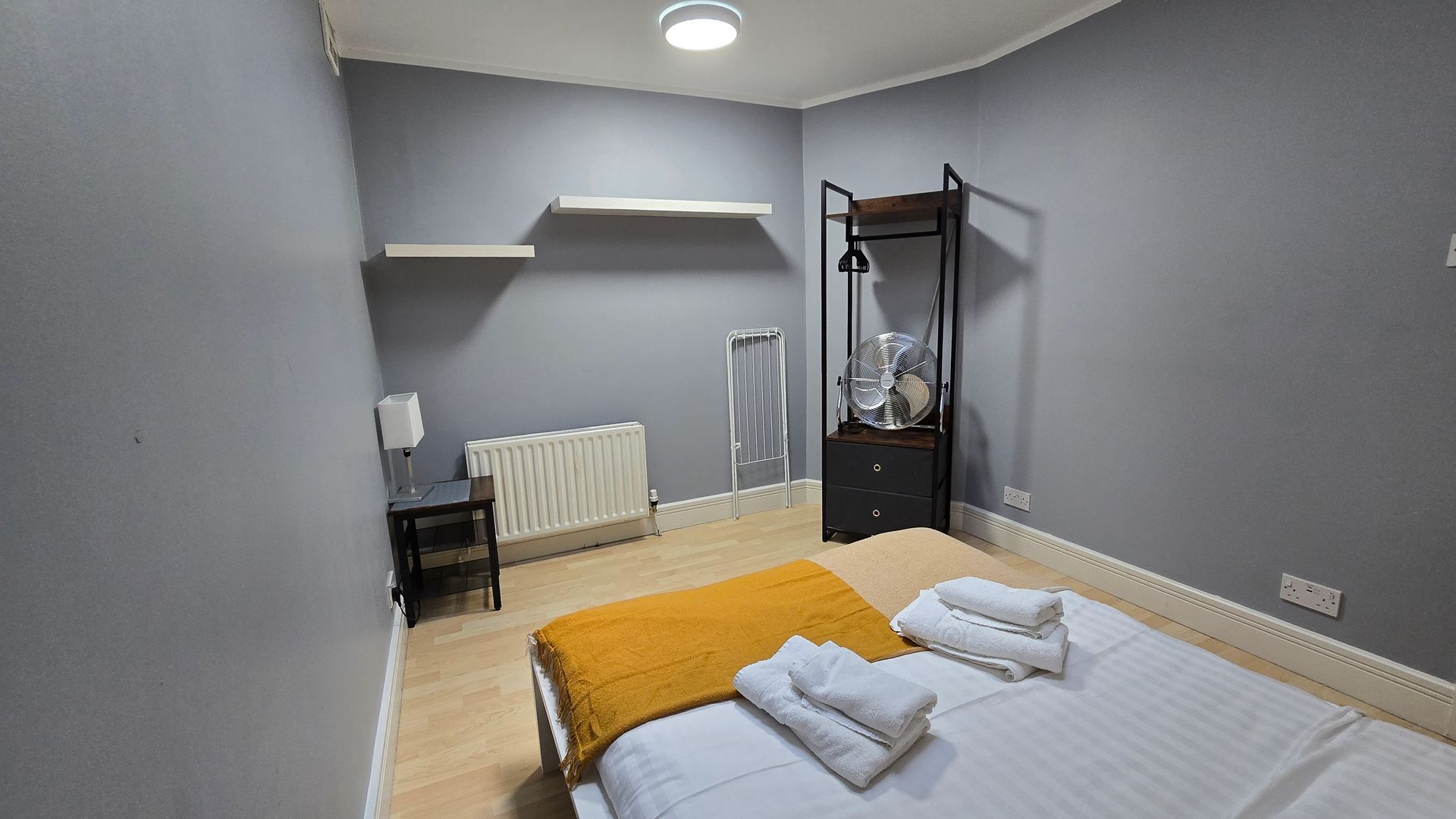 A bedroom with a bed , a dresser , a lamp , and a radiator.