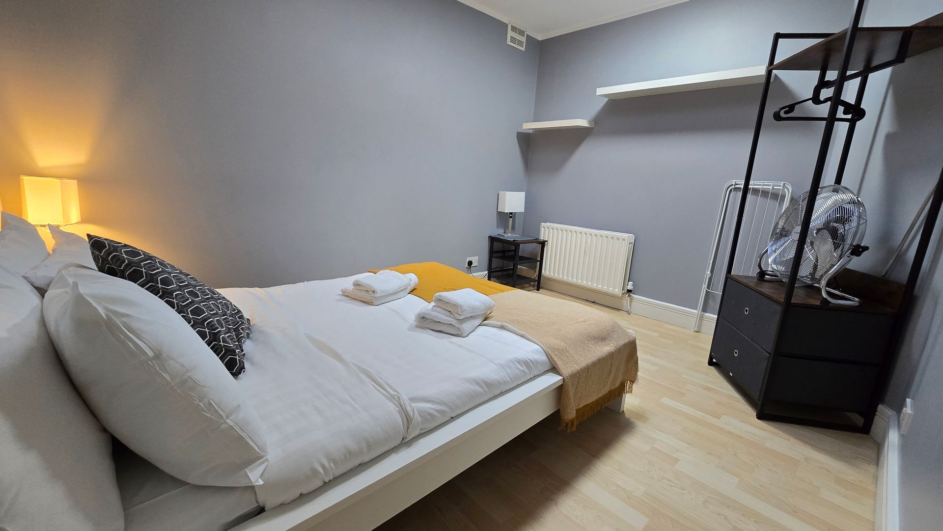 A bedroom with a bed , nightstand , dresser and fan.