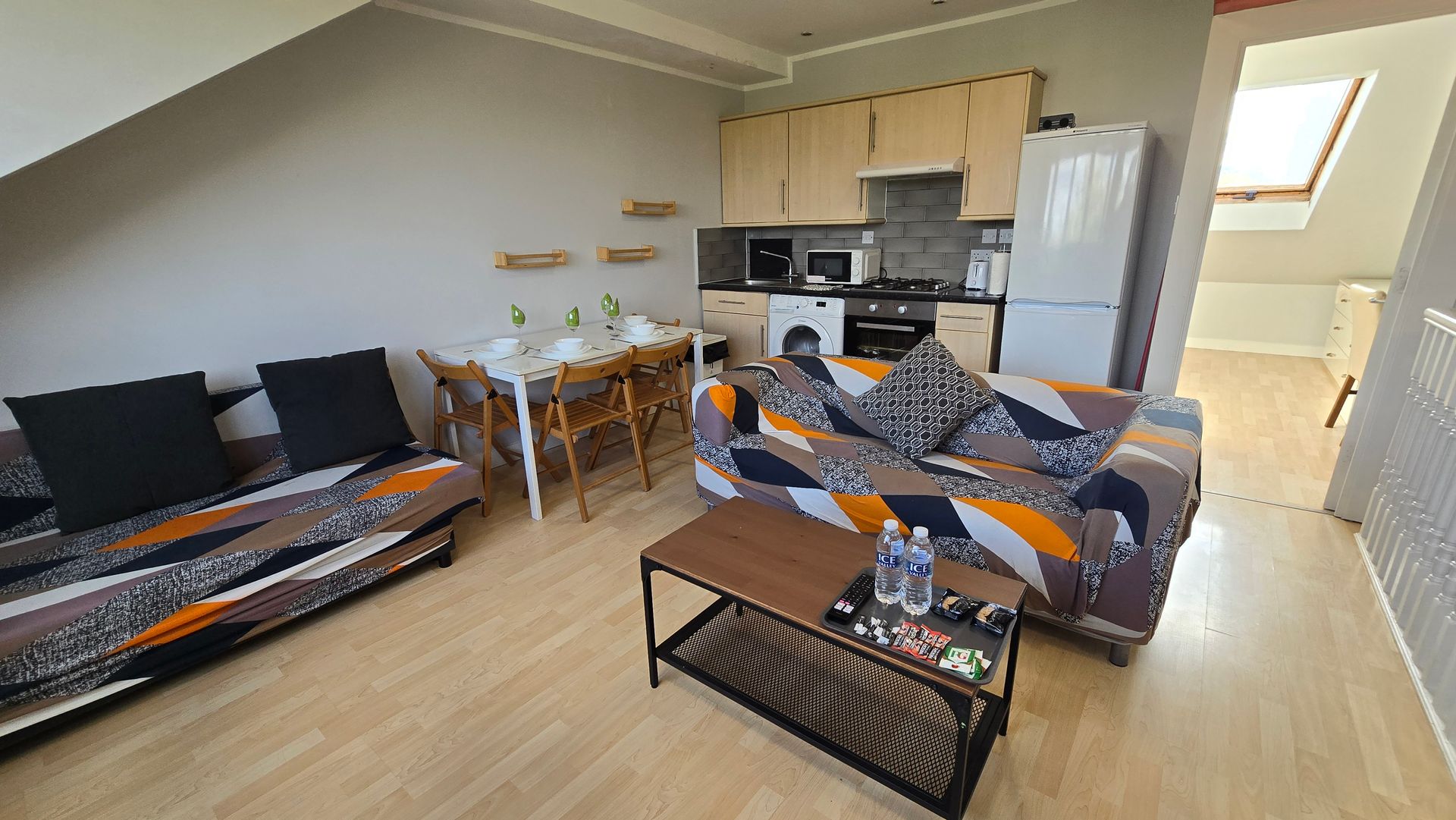 A living room with a couch , table , chairs and a refrigerator.