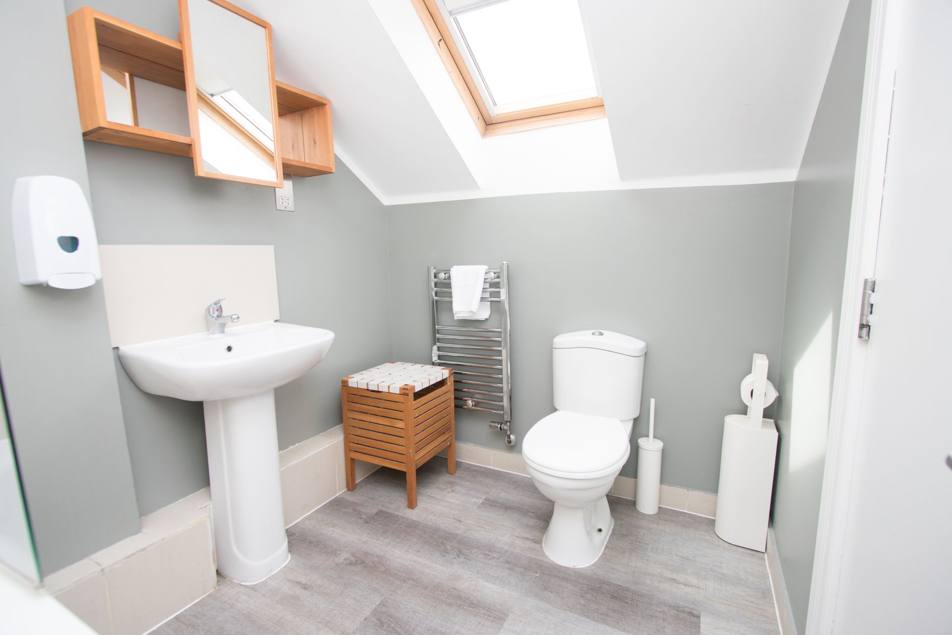 A bathroom with a toilet , sink , mirror and skylight.