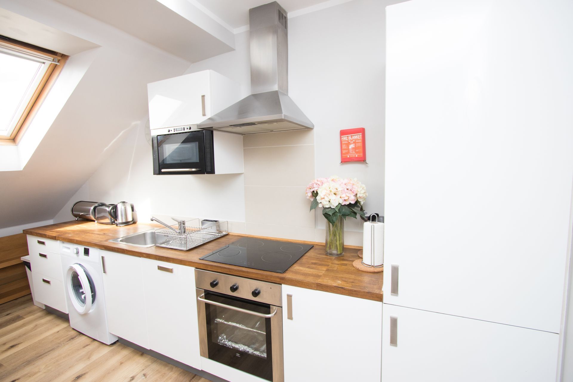 A kitchen with white cabinets , a stove , a washer and dryer , and a vase of flowers.
