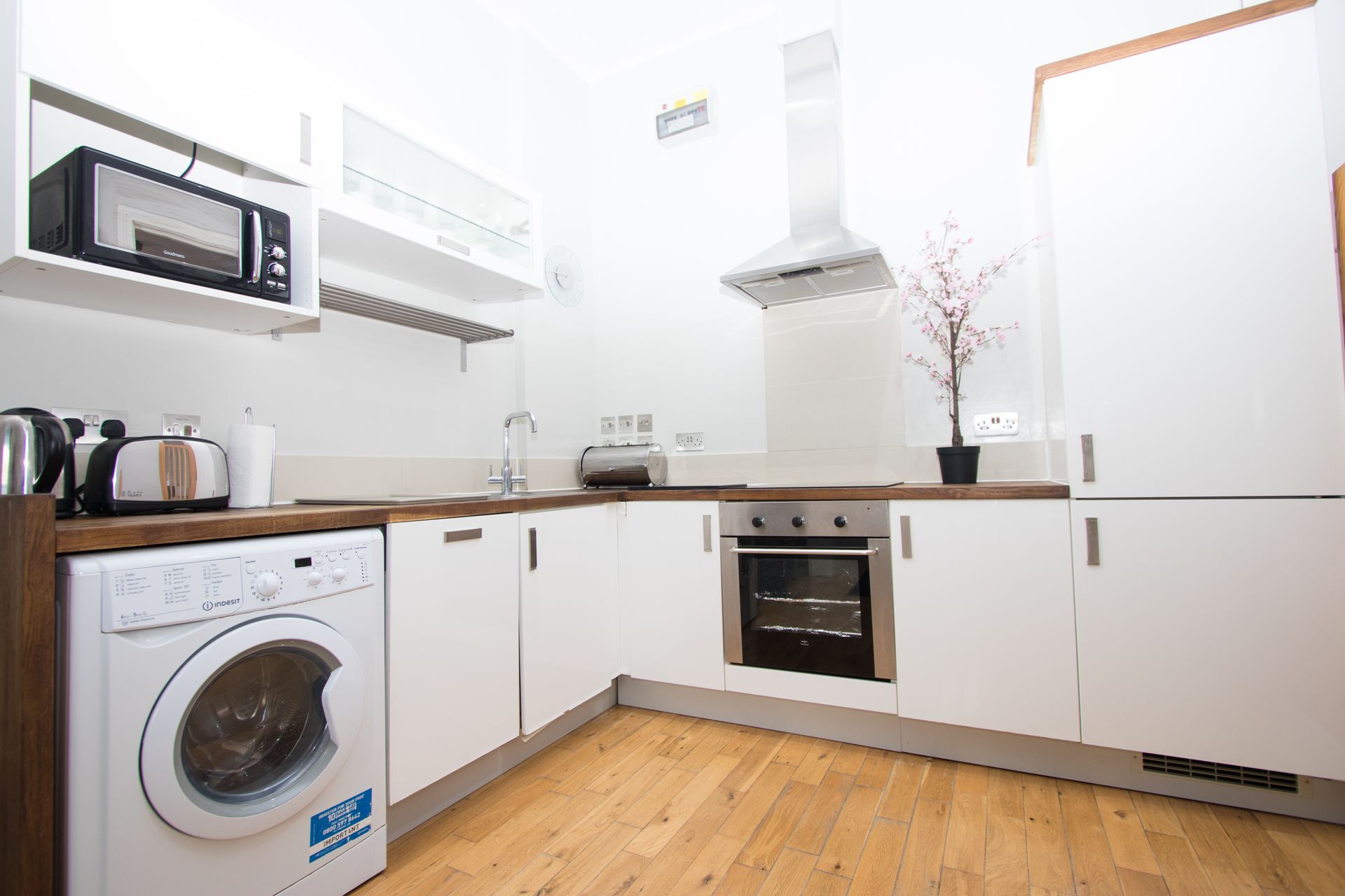 A kitchen with white cabinets , a washer and dryer , and a microwave.
