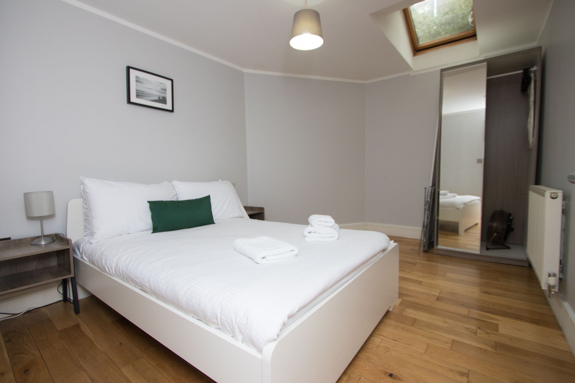 A bedroom with a bed , nightstand , lamp and a skylight.