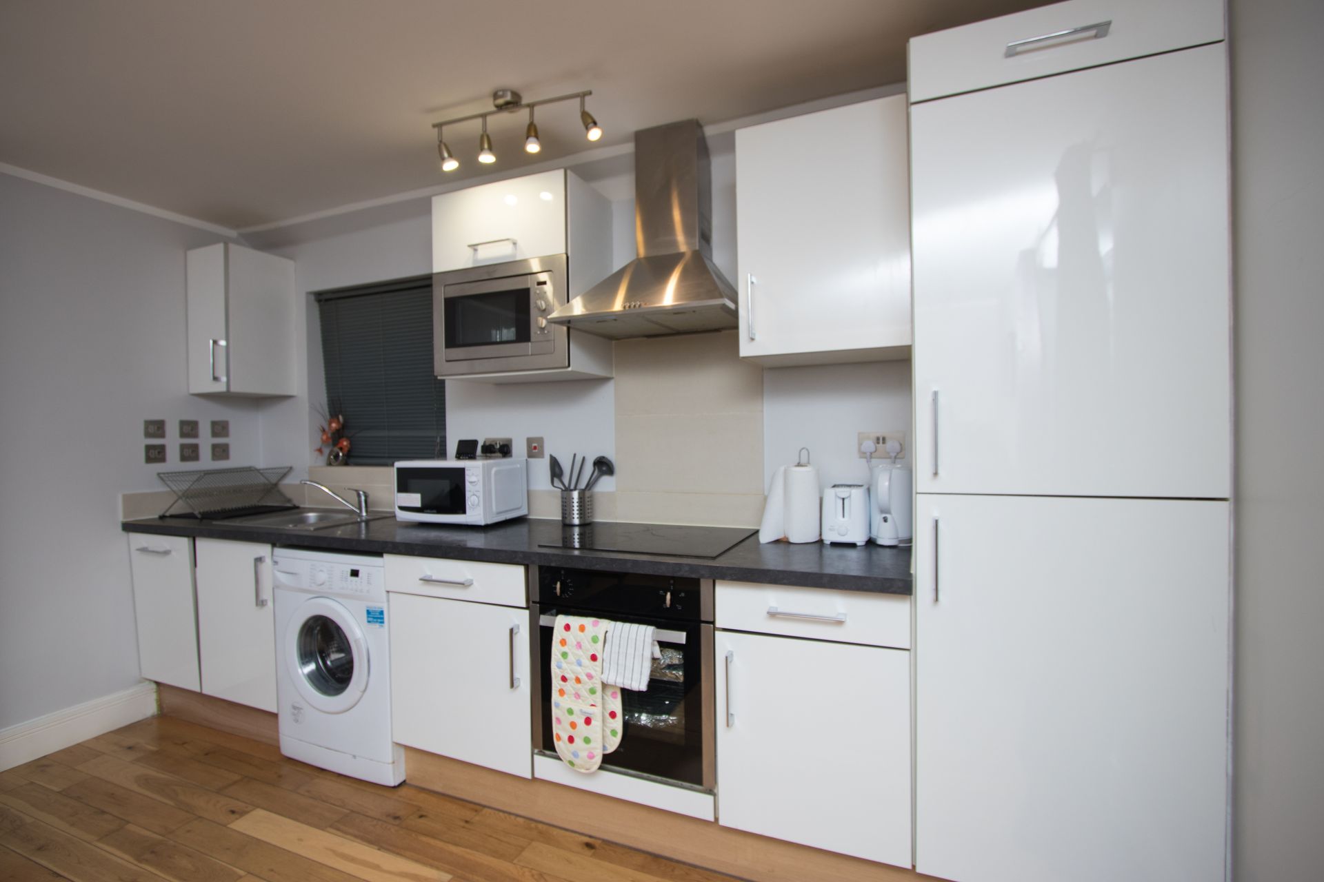 A kitchen with white cabinets , a refrigerator , a washing machine , and a microwave.