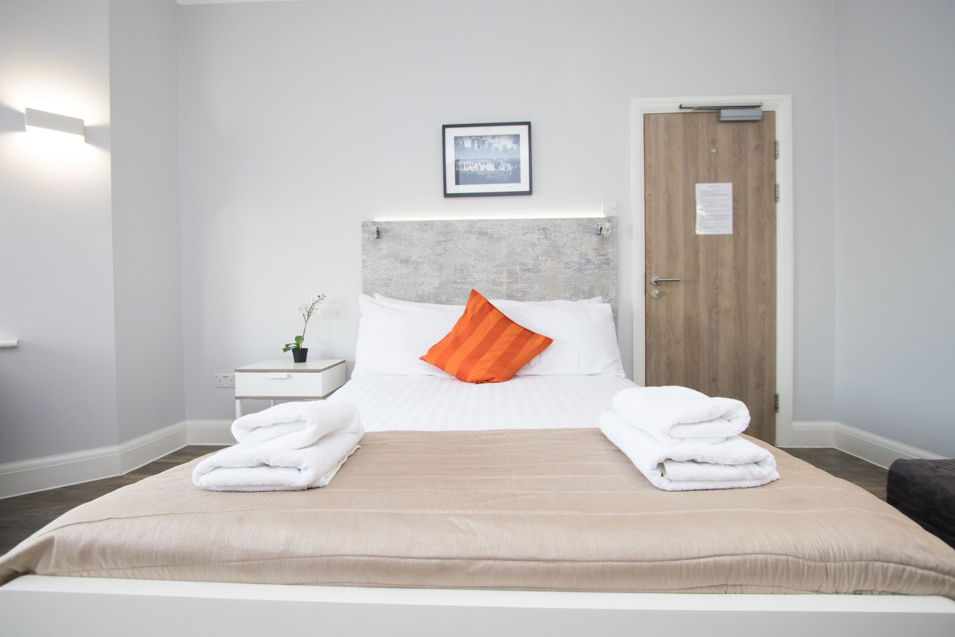 A hotel room with a bed , nightstand , towels and a door.