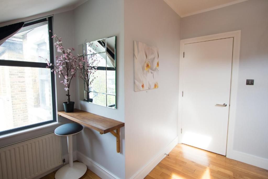 A room with a window , a stool , a shelf , a mirror and a door.