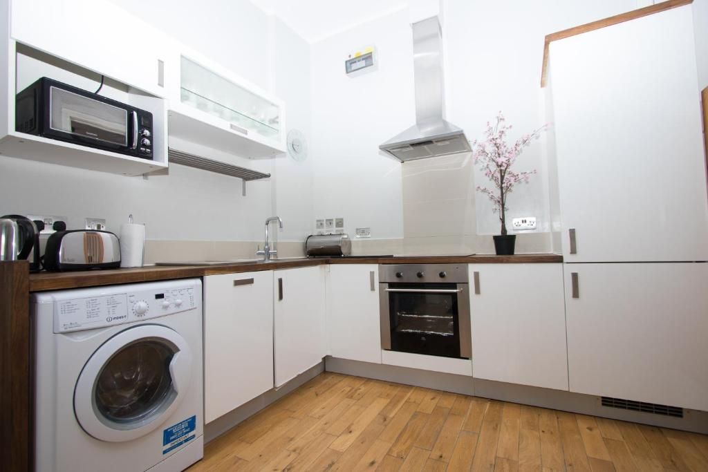 A kitchen with white cabinets , a washer and dryer , and a microwave.