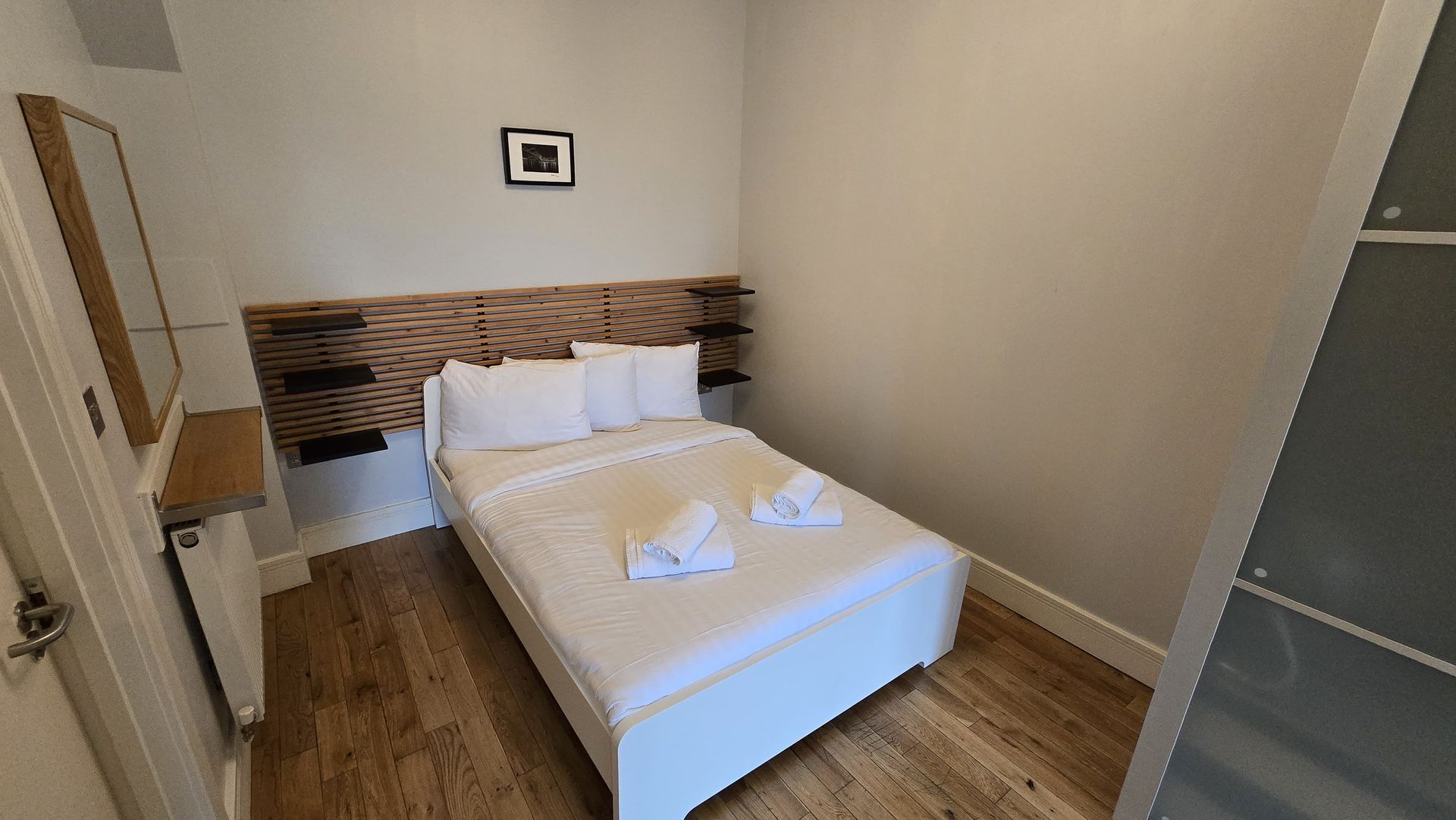A bedroom with a bed , mirror , and wooden floor.