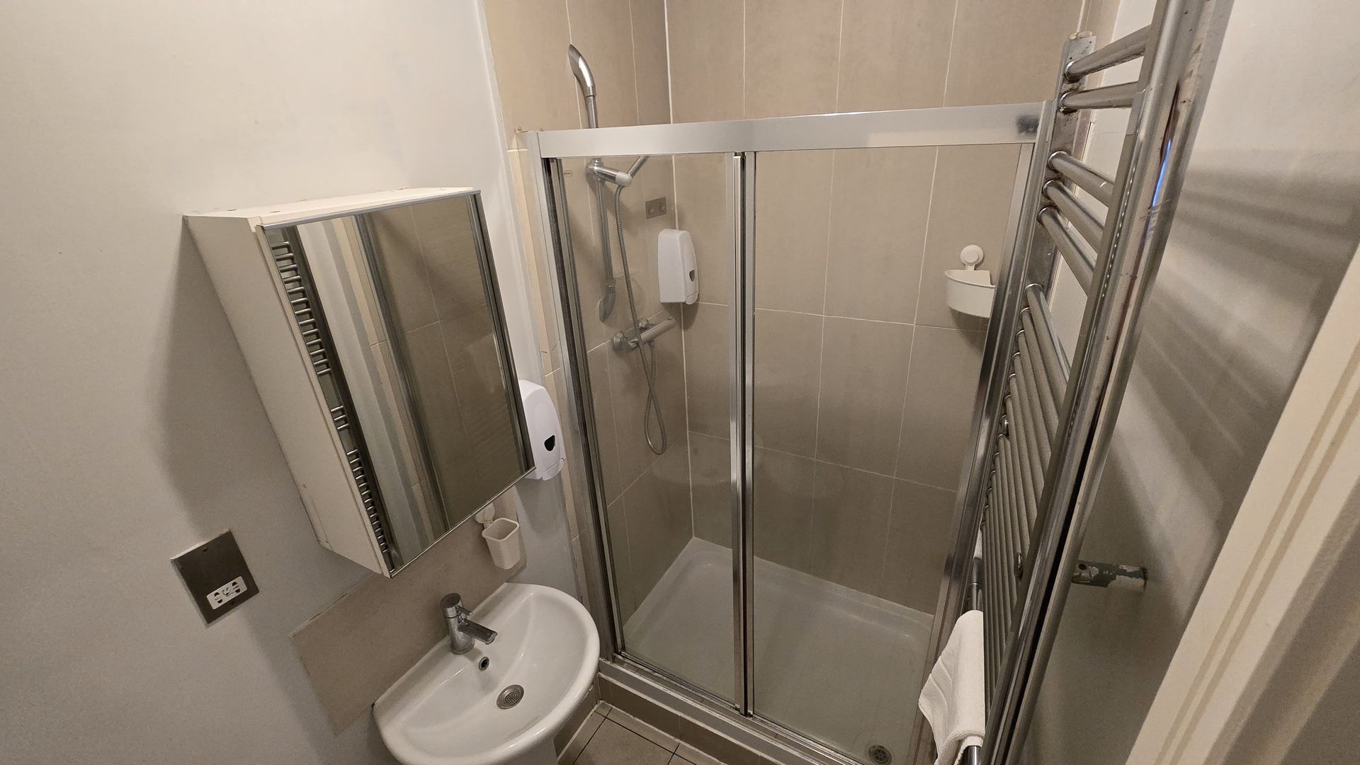A bathroom with a shower , sink , mirror and towel rack.