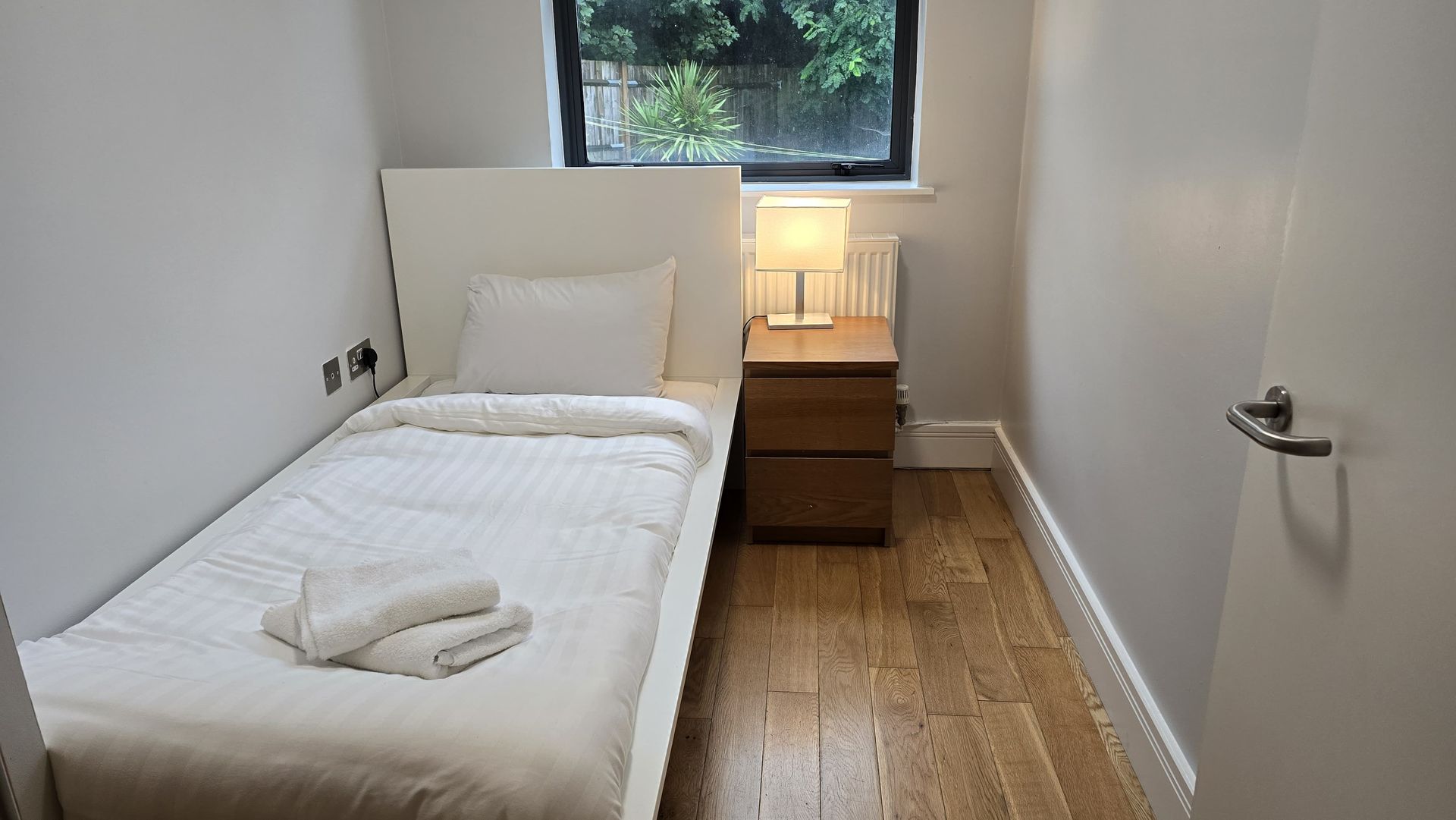 A bedroom with a single bed , nightstand , and window.
