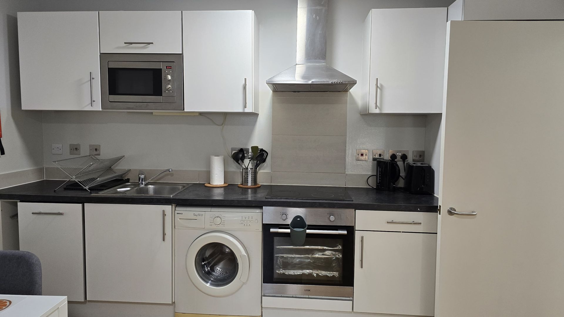 A kitchen with white cabinets , a washer and dryer , an oven , and a microwave.