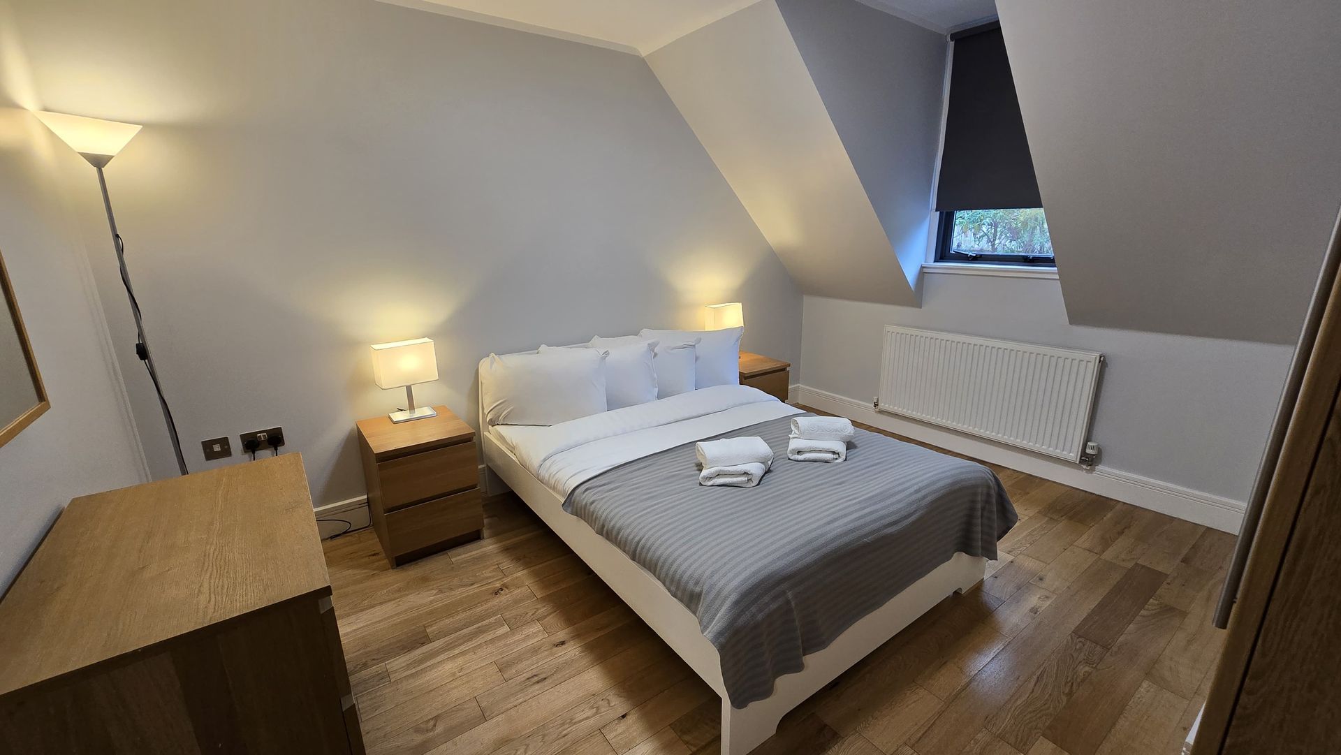 A bedroom with a bed , two nightstands , a mirror and a window.