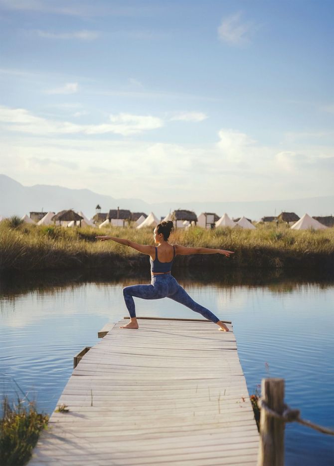 Una mujer está haciendo yoga en un muelle junto a un lago.