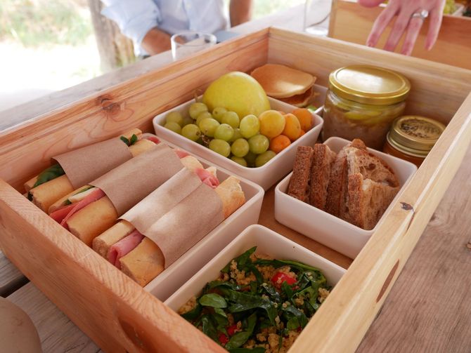 Una caja de madera llena de sándwiches, ensaladas, frutas y pan.