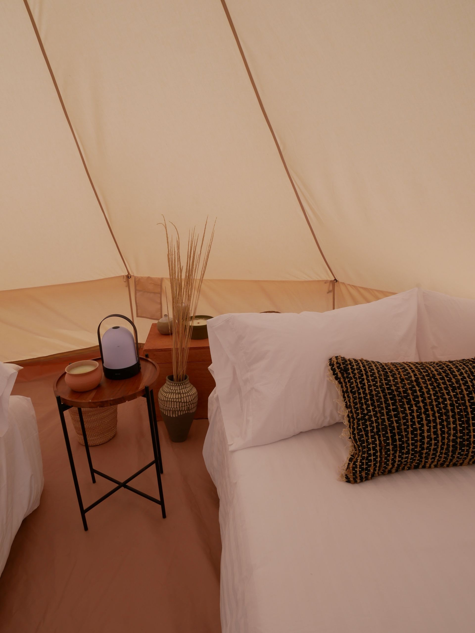 Una tienda de campaña con dos camas y una mesa con una lámpara encima.