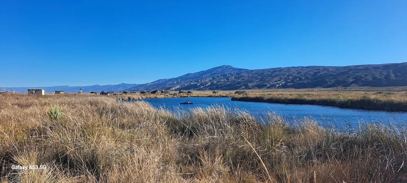 Hay un lago en el medio de un campo con montañas al fondo.
