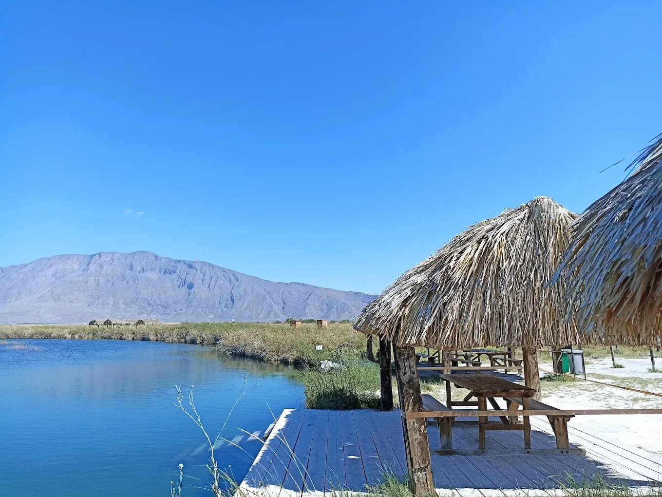 Una mesa de picnic está situada en un muelle junto a un lago con montañas al fondo.