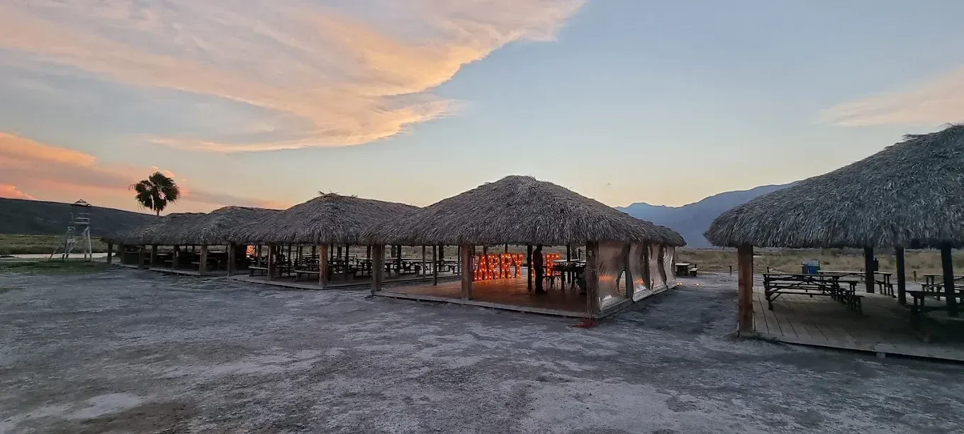 Una hilera de chozas con techo de paja y una puesta de sol al fondo.