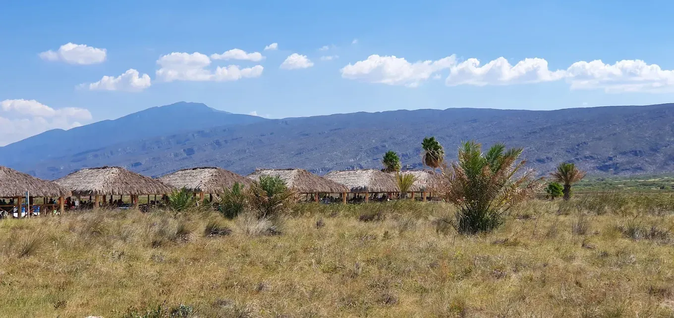 Un campo con una montaña al fondo y unas cuantas chozas en primer plano.