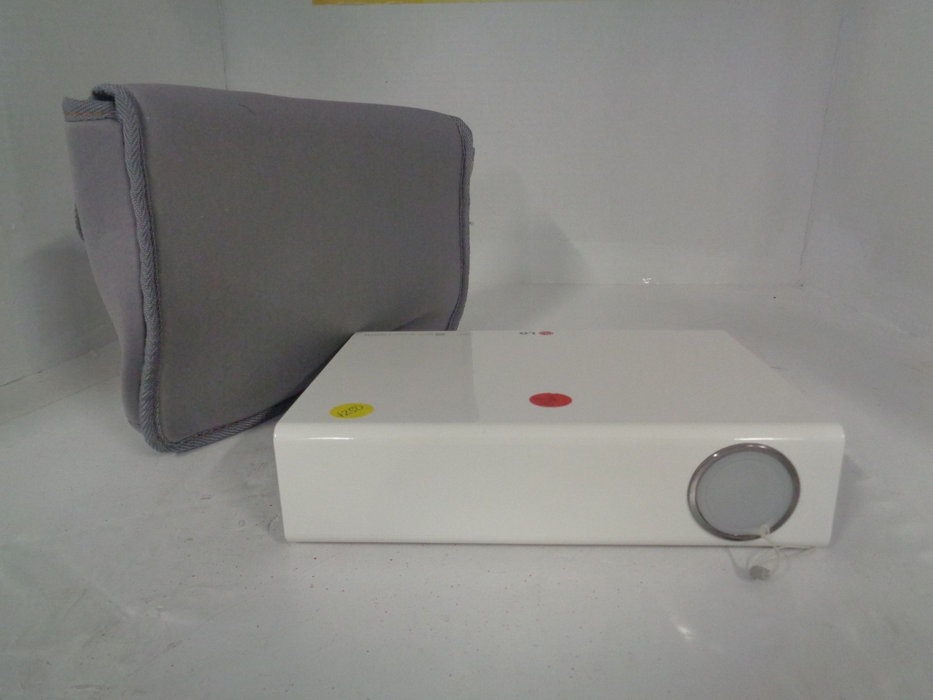 White projector and gray carrying case on a white surface. The projector has a red and yellow dot on top and a silver lens.
