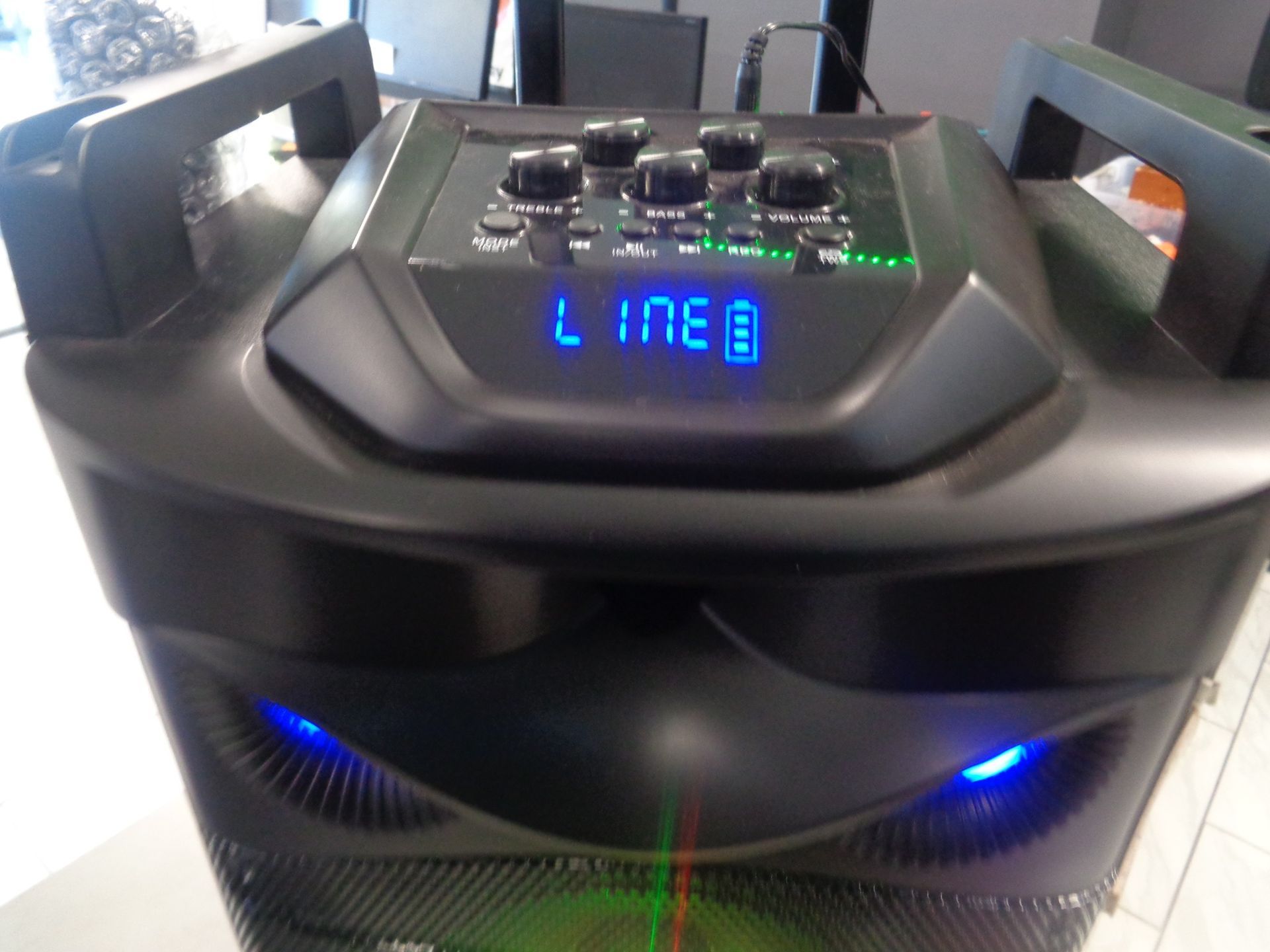 Black speaker with control panel, blue lights, and handles; displays 