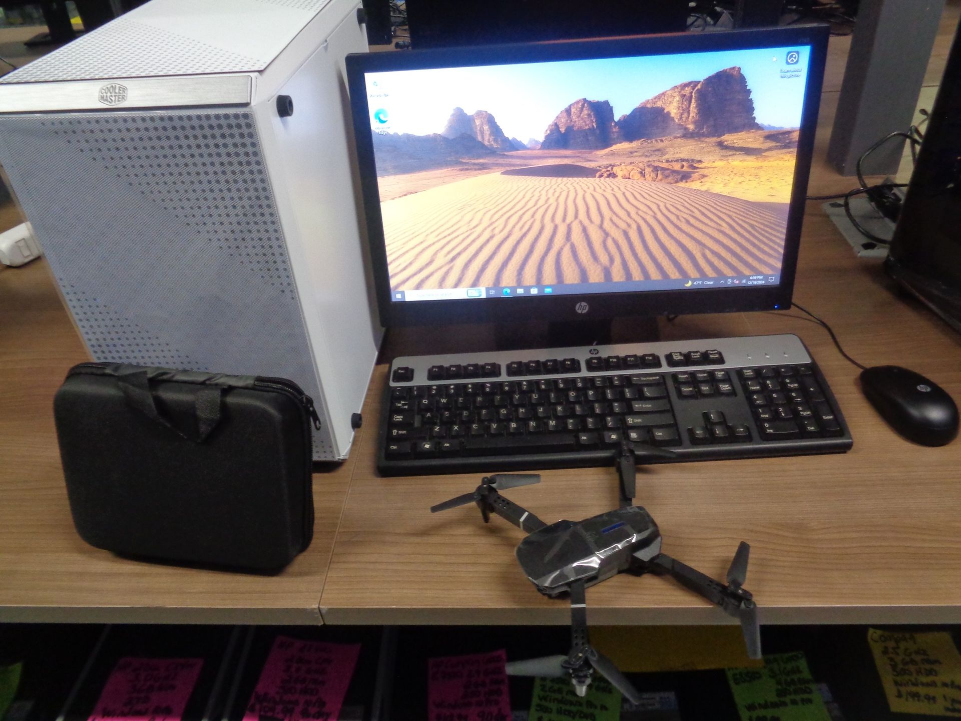 Desktop computer with a drone, keyboard, mouse, and a black case on a desk.