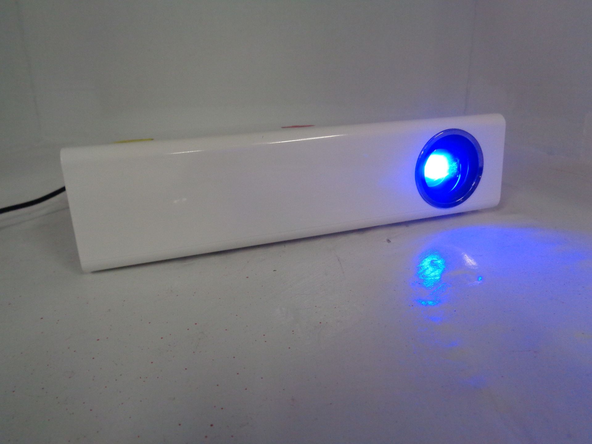 White projector with a bright blue light shining from its lens onto a surface.