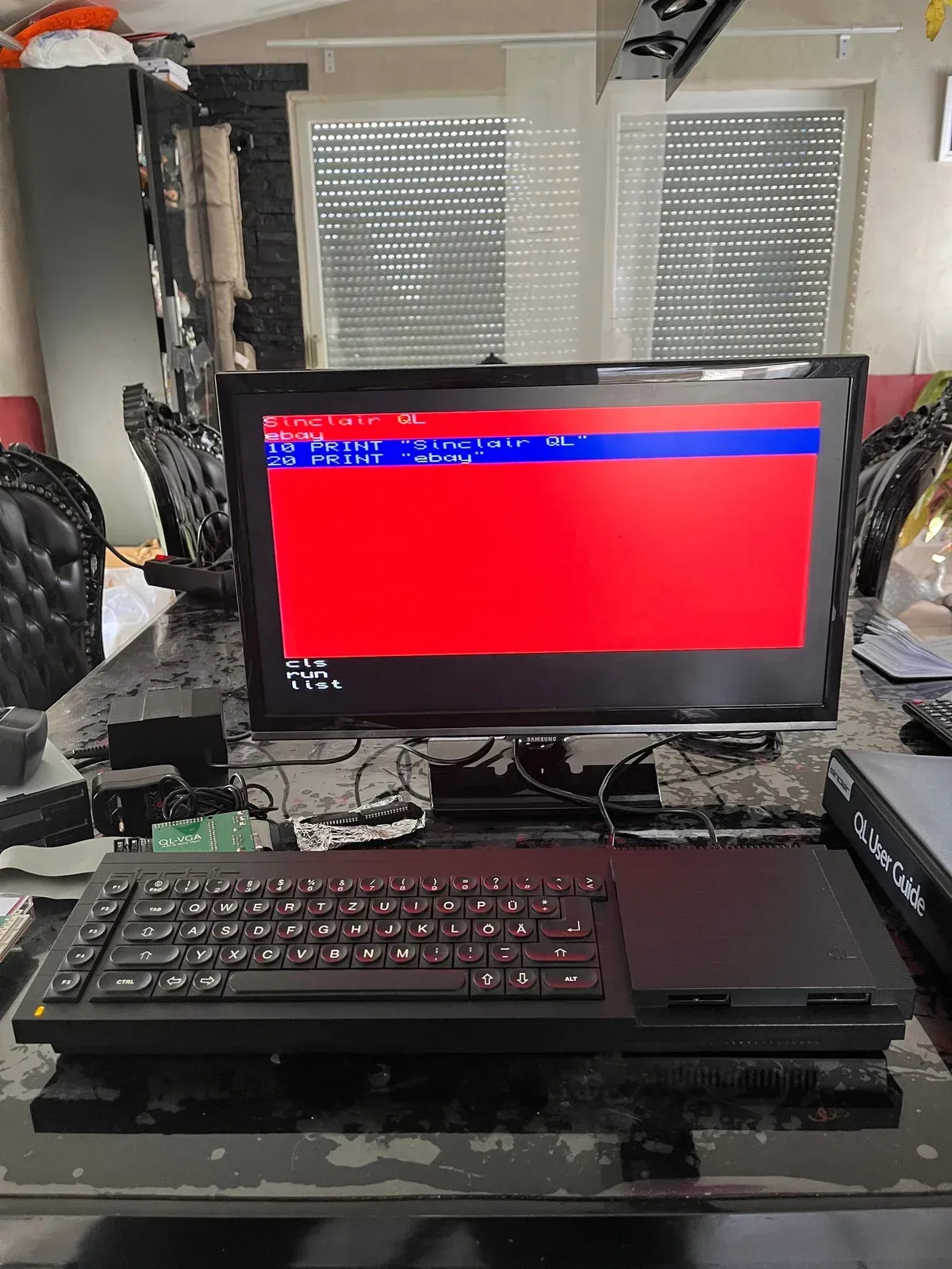 A computer setup on a table. A red screen with blue lines, keyboard, and monitor.