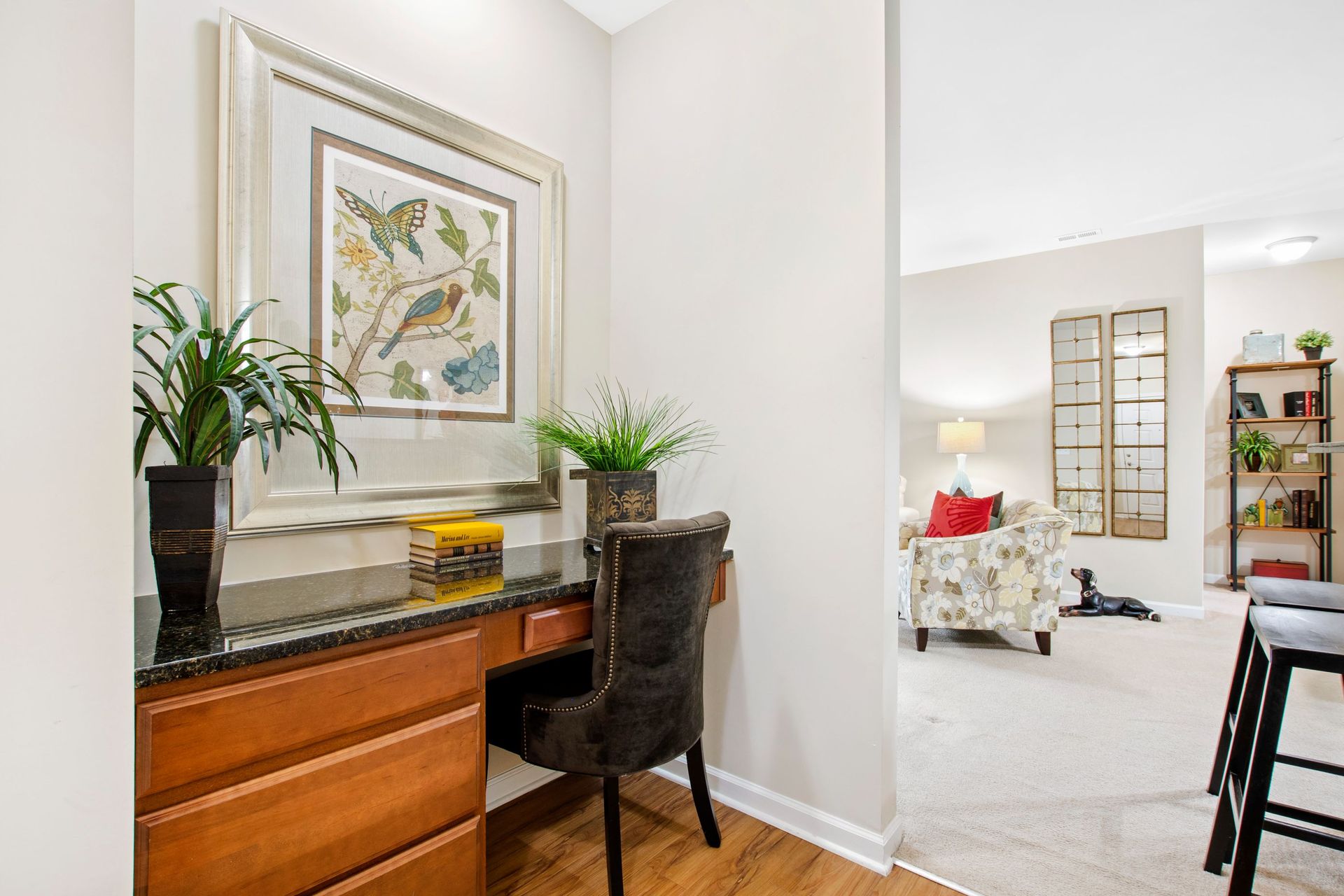 Home office nook with granite countertop, potted plants, and framed artwork in a living area.