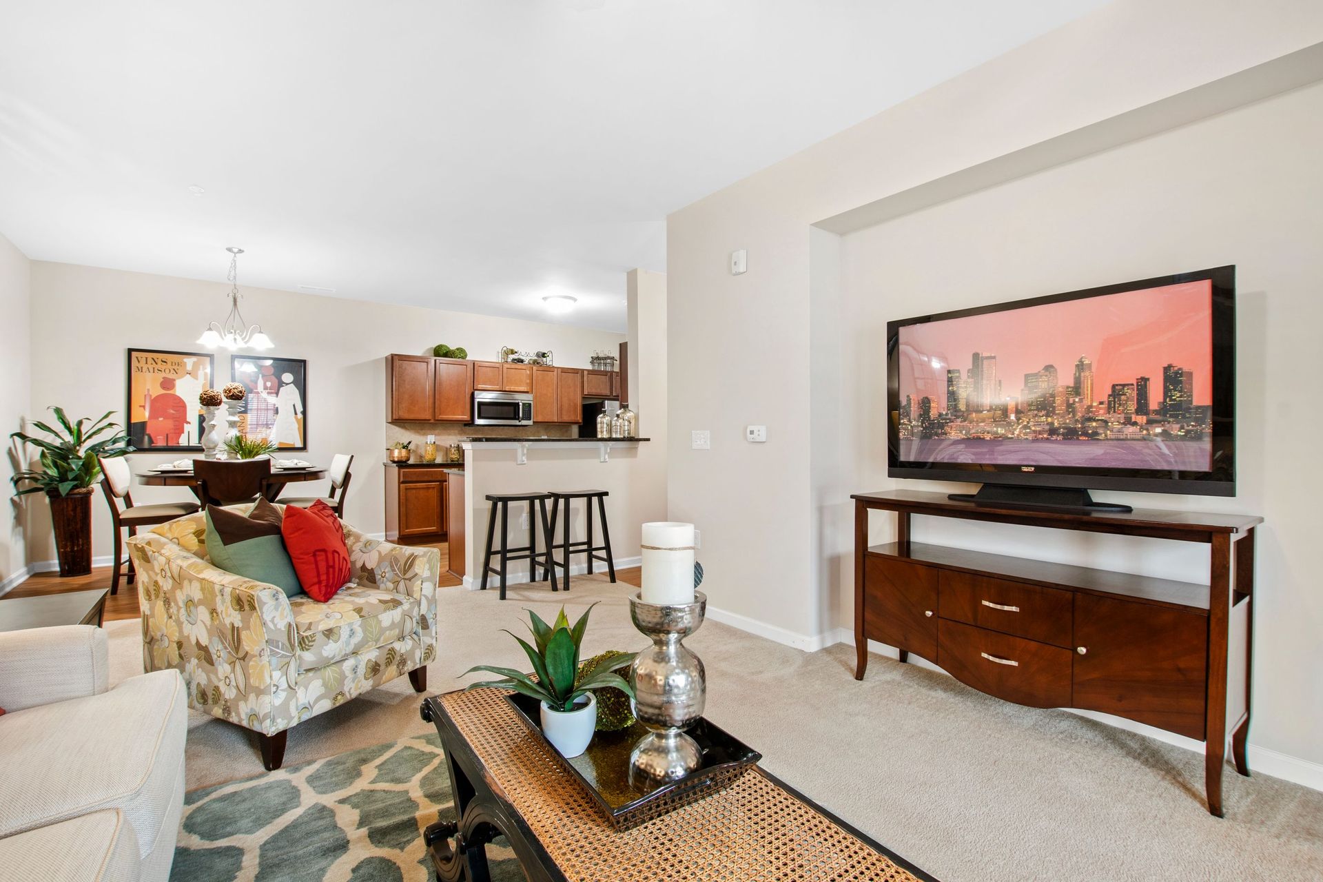 Open-concept living room with sofa, coffee table, TV on a console, and a kitchen with bar stools.