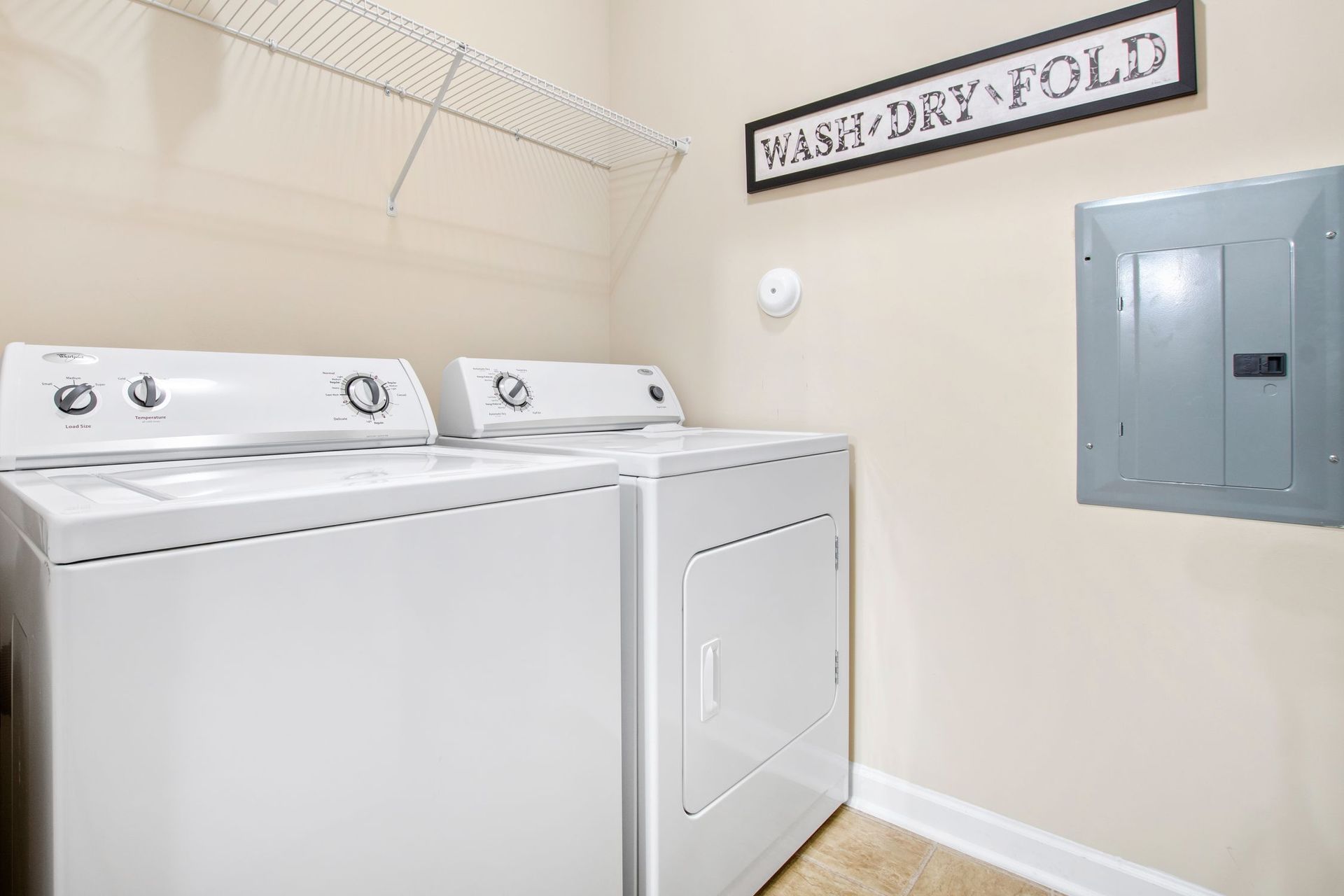 Laundry room with white washer and dryer side by side and a 'WASH DRY FOLD' sign.