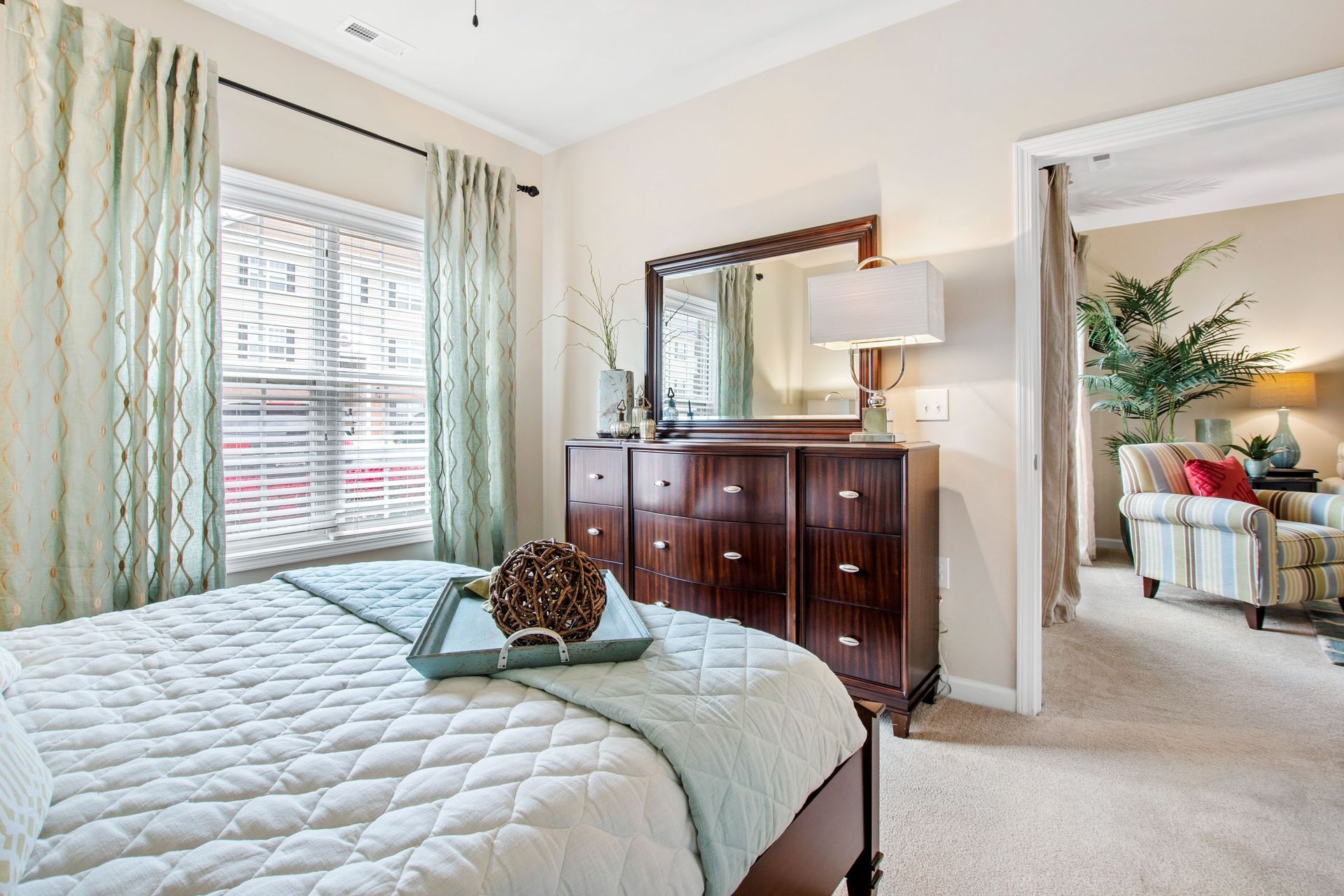 Bedroom with a bed, dark wood dresser with mirror, and mint curtains by a window.