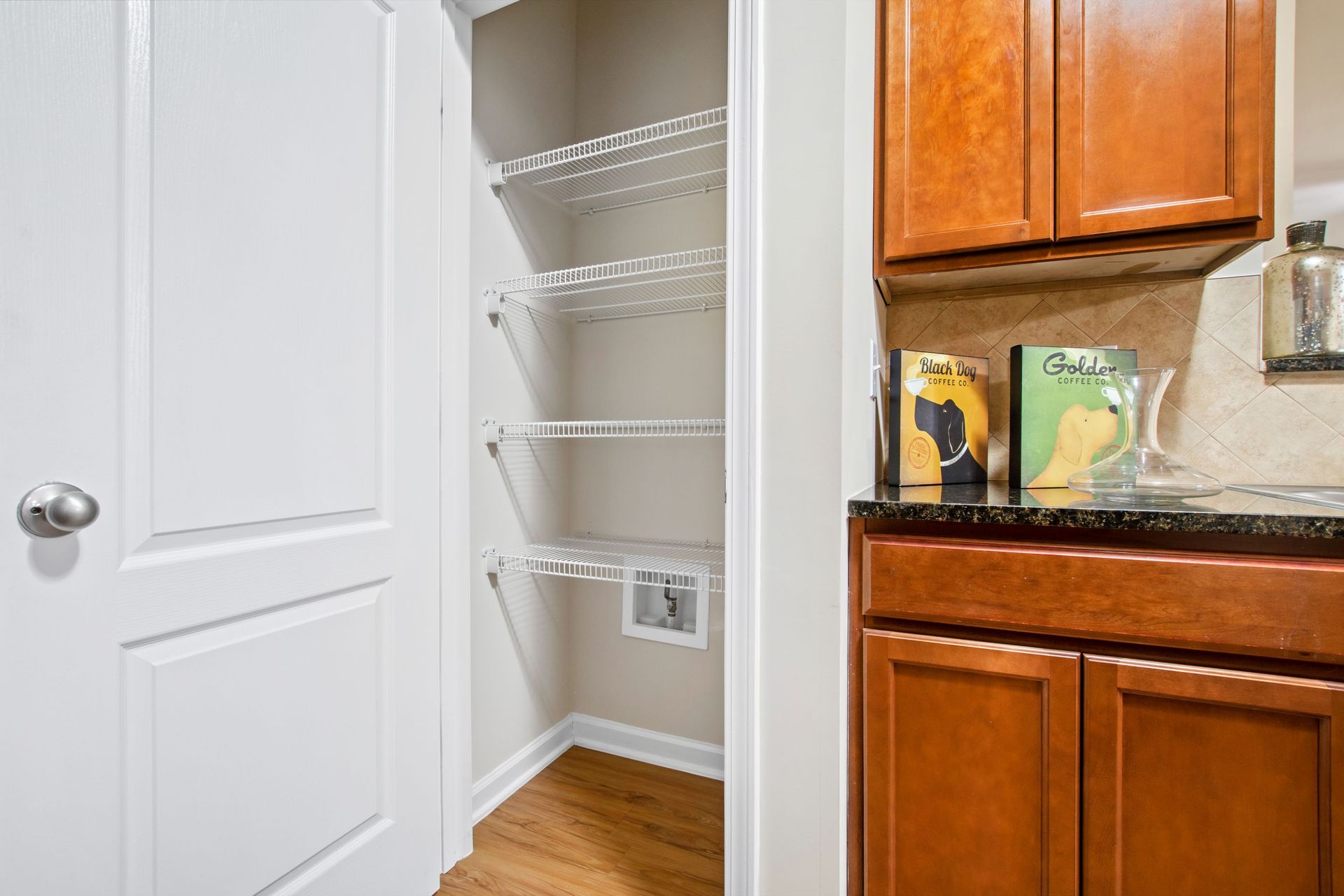 Pantry closet with white wire shelves and open door beside kitchen cabinets.