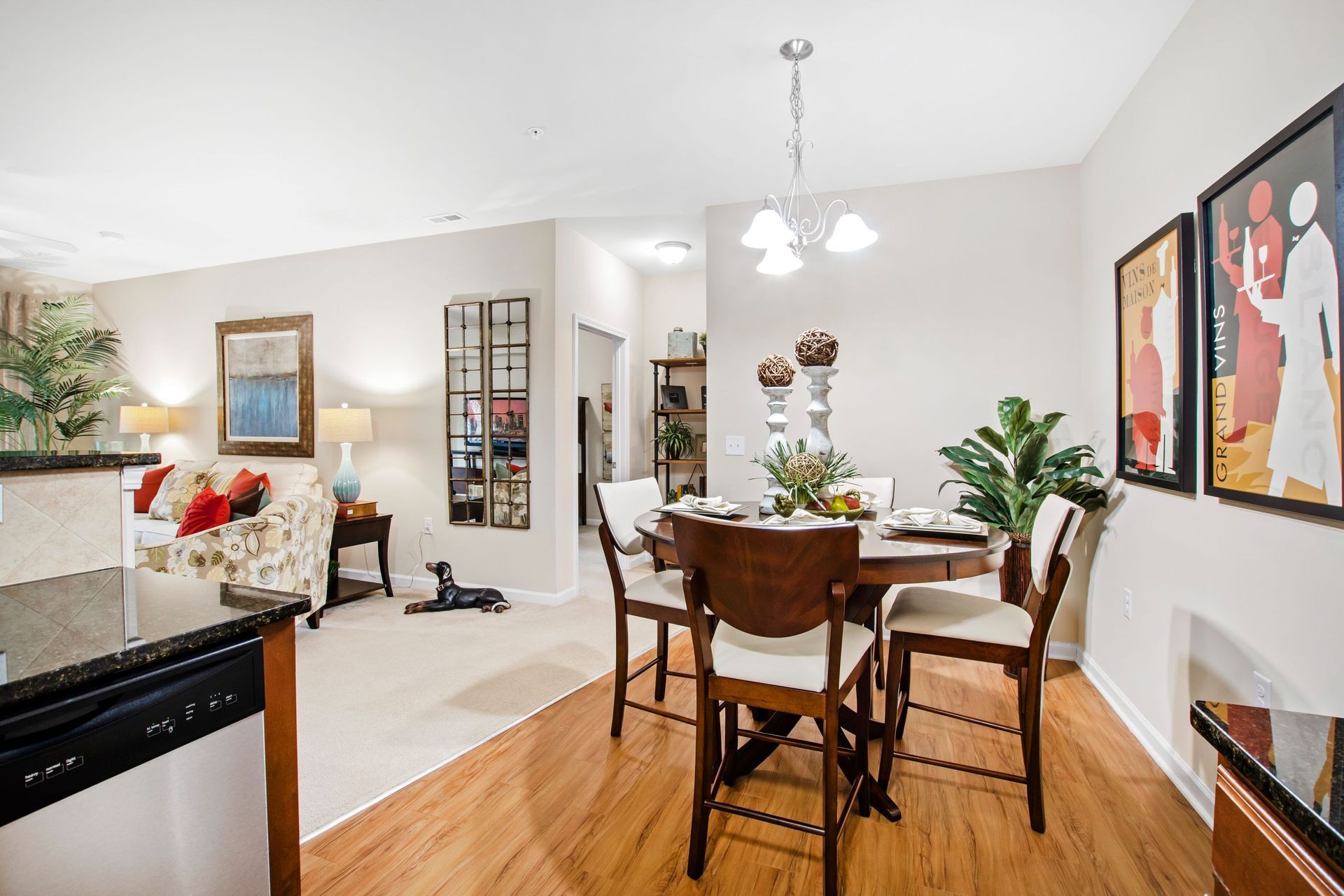 Open-concept apartment dining area with a round wooden table and cream chairs in a bright space.