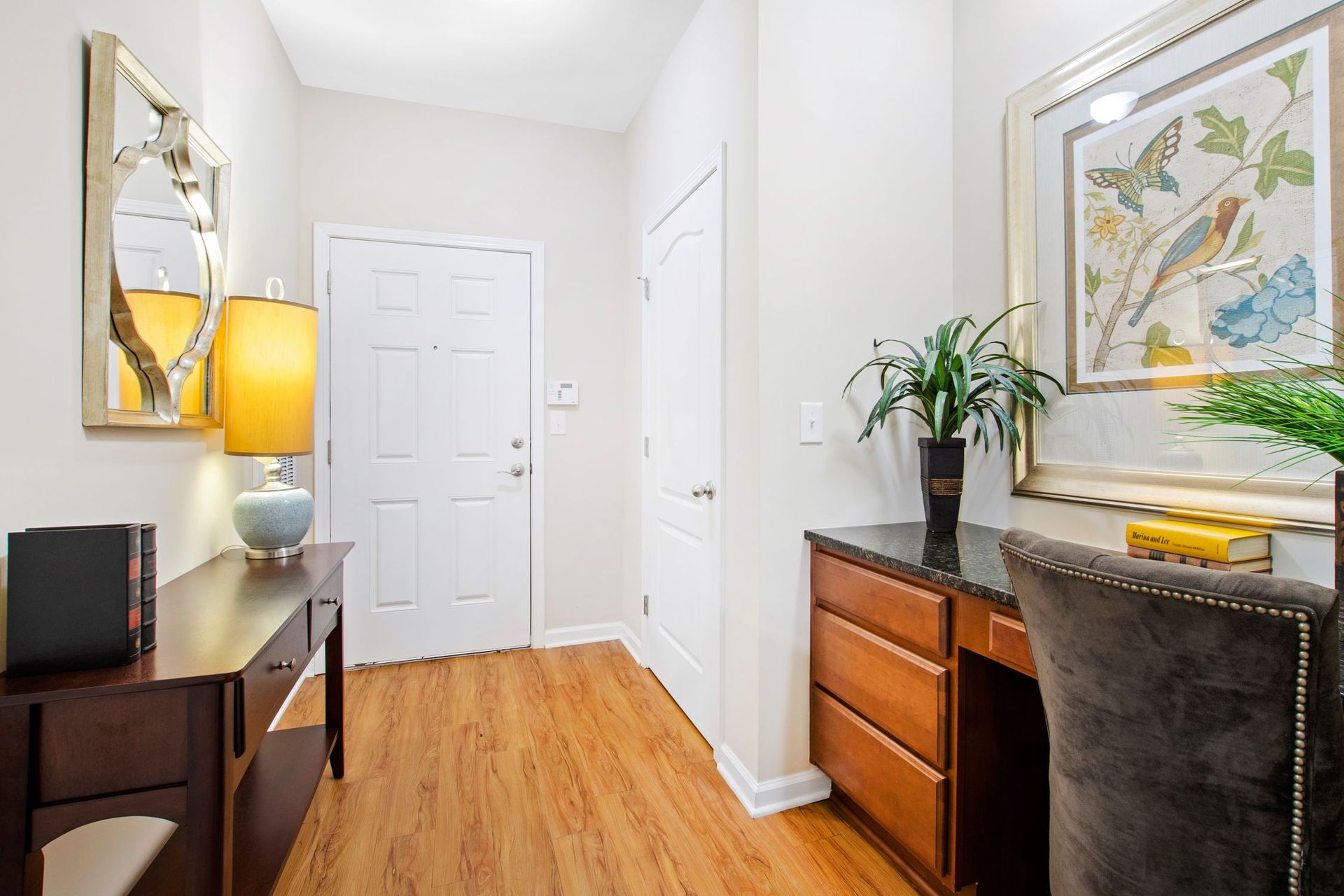 Entryway with a desk, chair, lamp, and framed wall art in a neutral hallway.