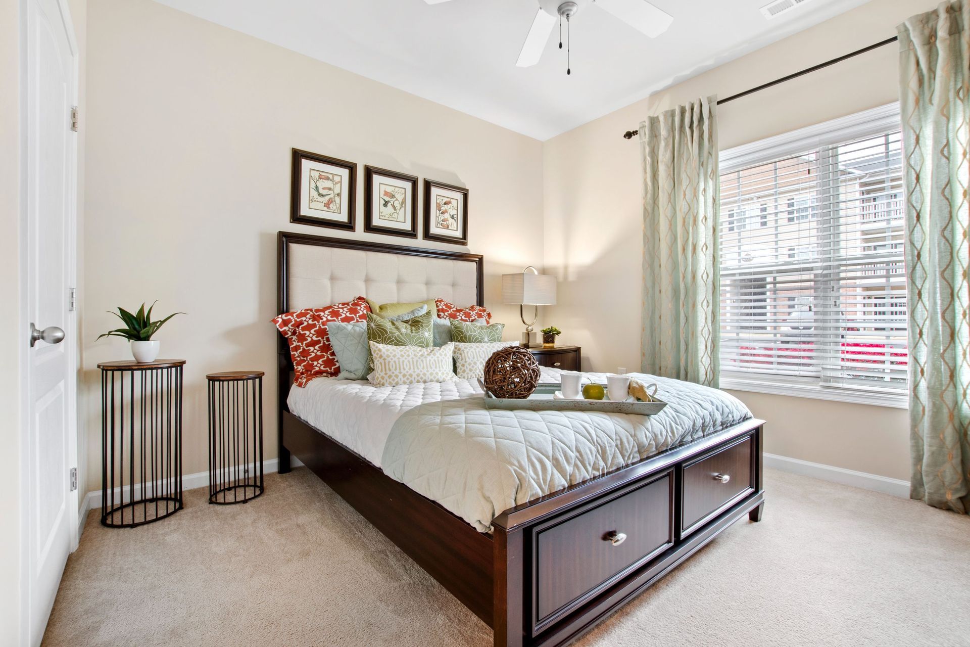 Bedroom in an apartment with a dark wood bed, tufted headboard, and a window with blinds.
