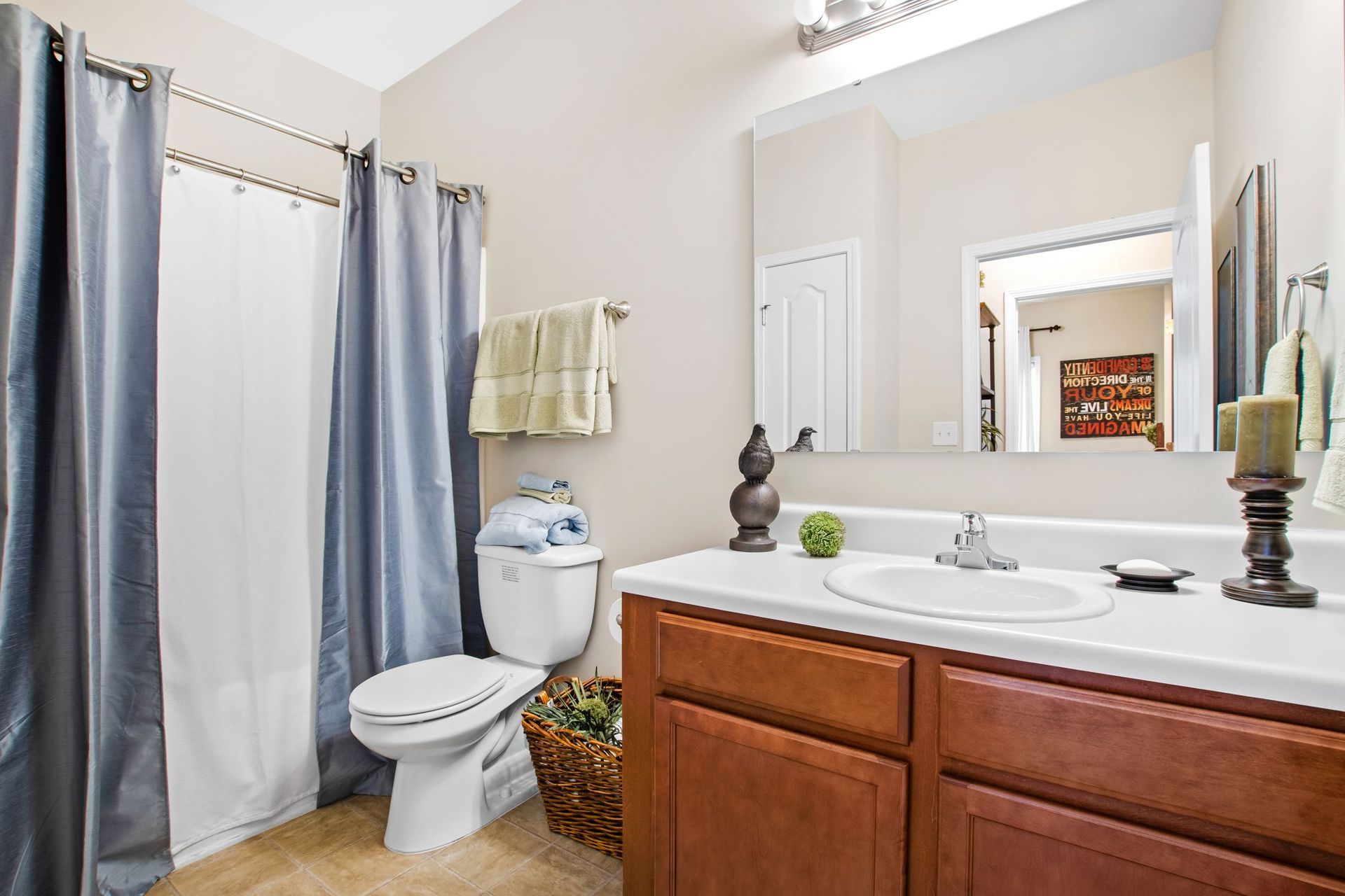 Bathroom with white toilet and sink, large mirror, and blue-gray shower curtain.
