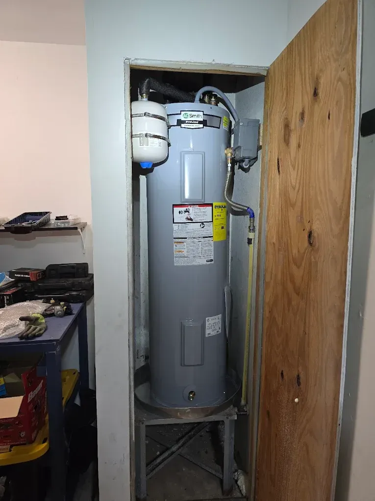 A water heater is sitting in a closet next to a wooden door.