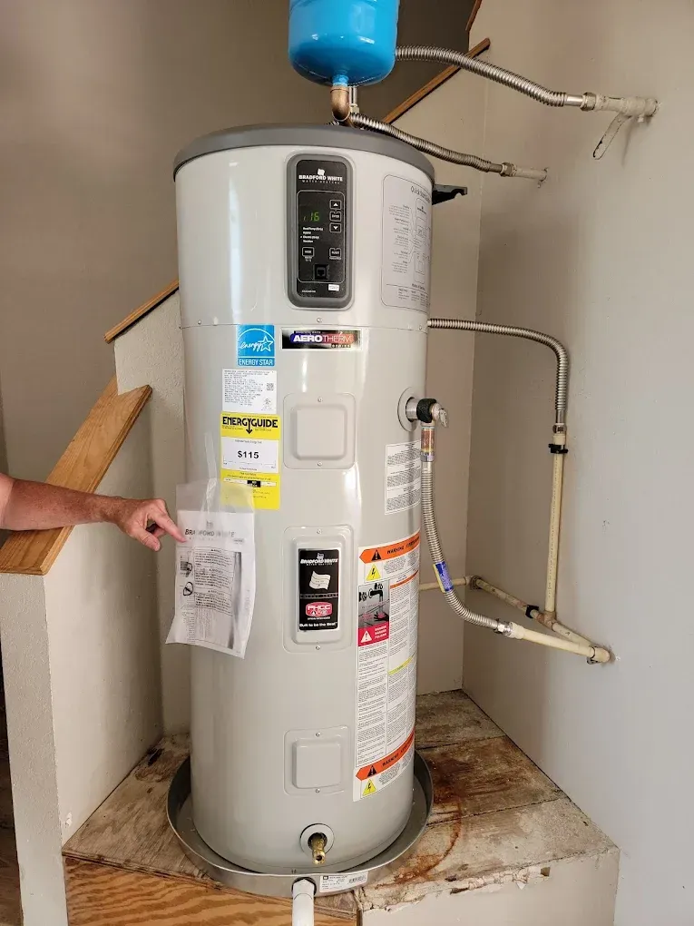 A person is standing next to a water heater in a room.