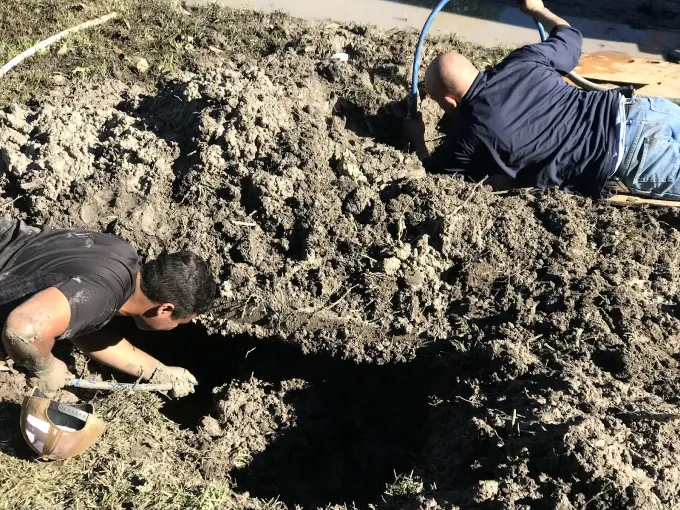 Two men are digging a hole in the dirt.