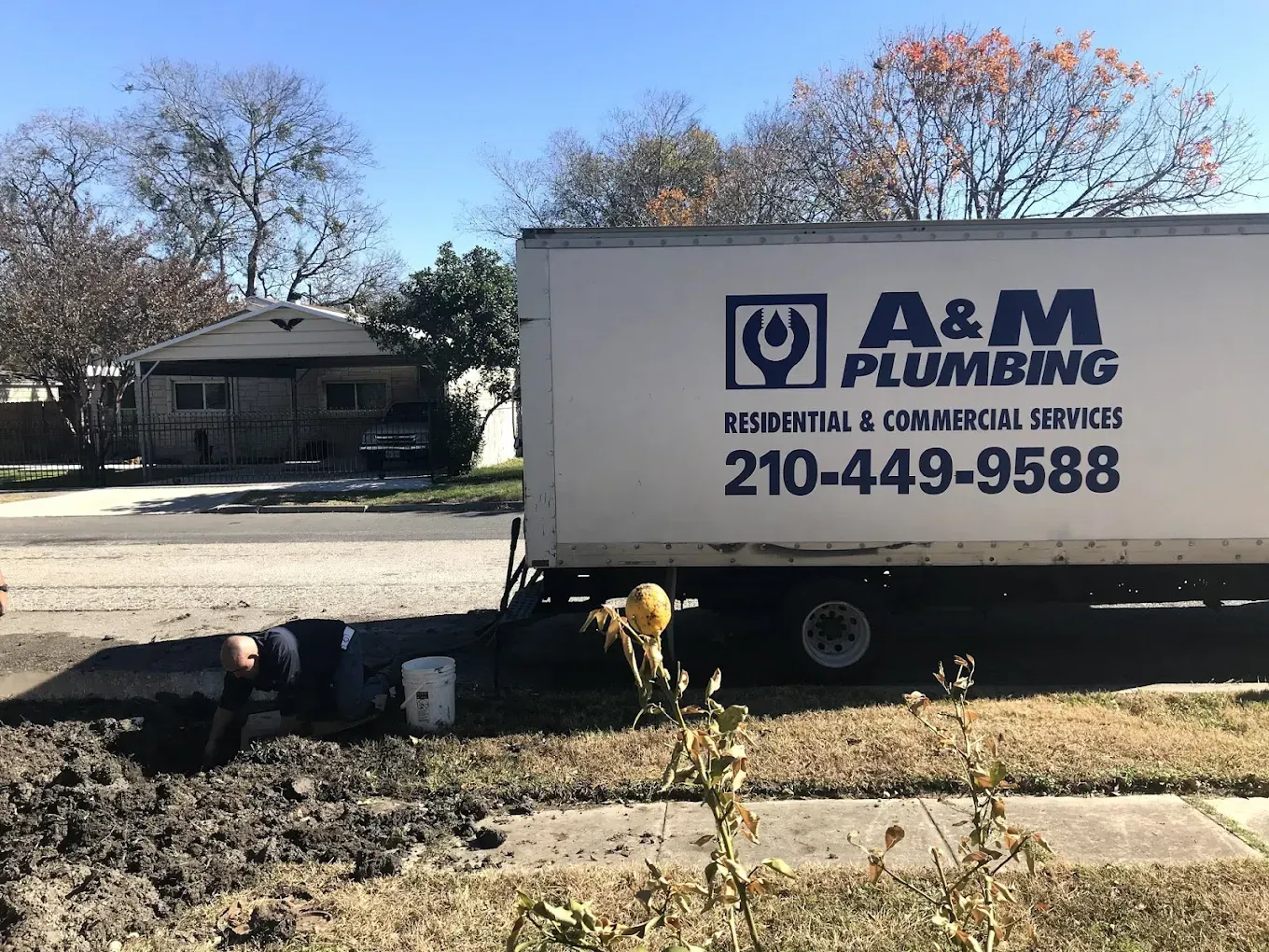A white a & m plumbing truck is parked in front of a house