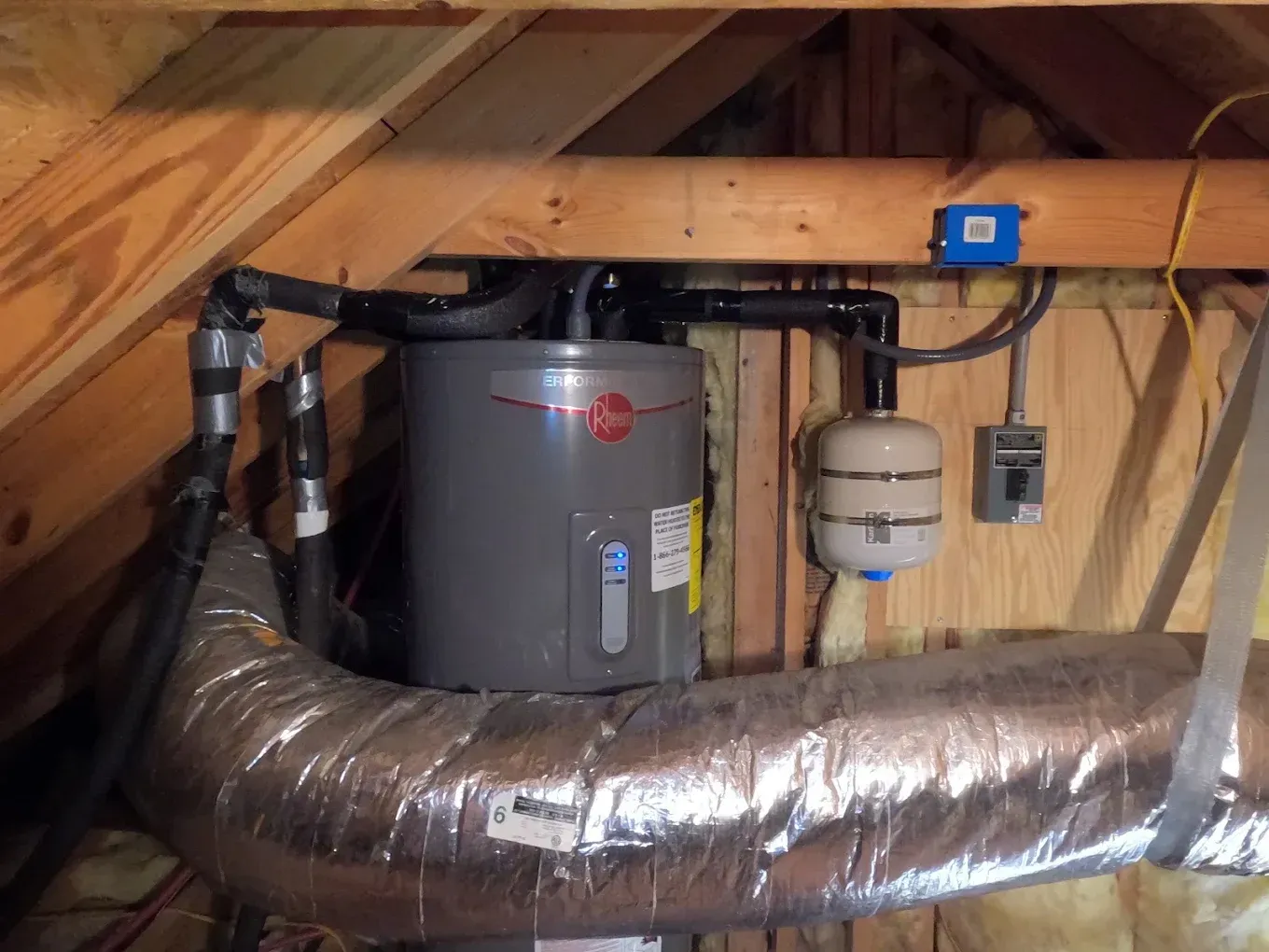 A gray water heater is hanging from the ceiling of an attic